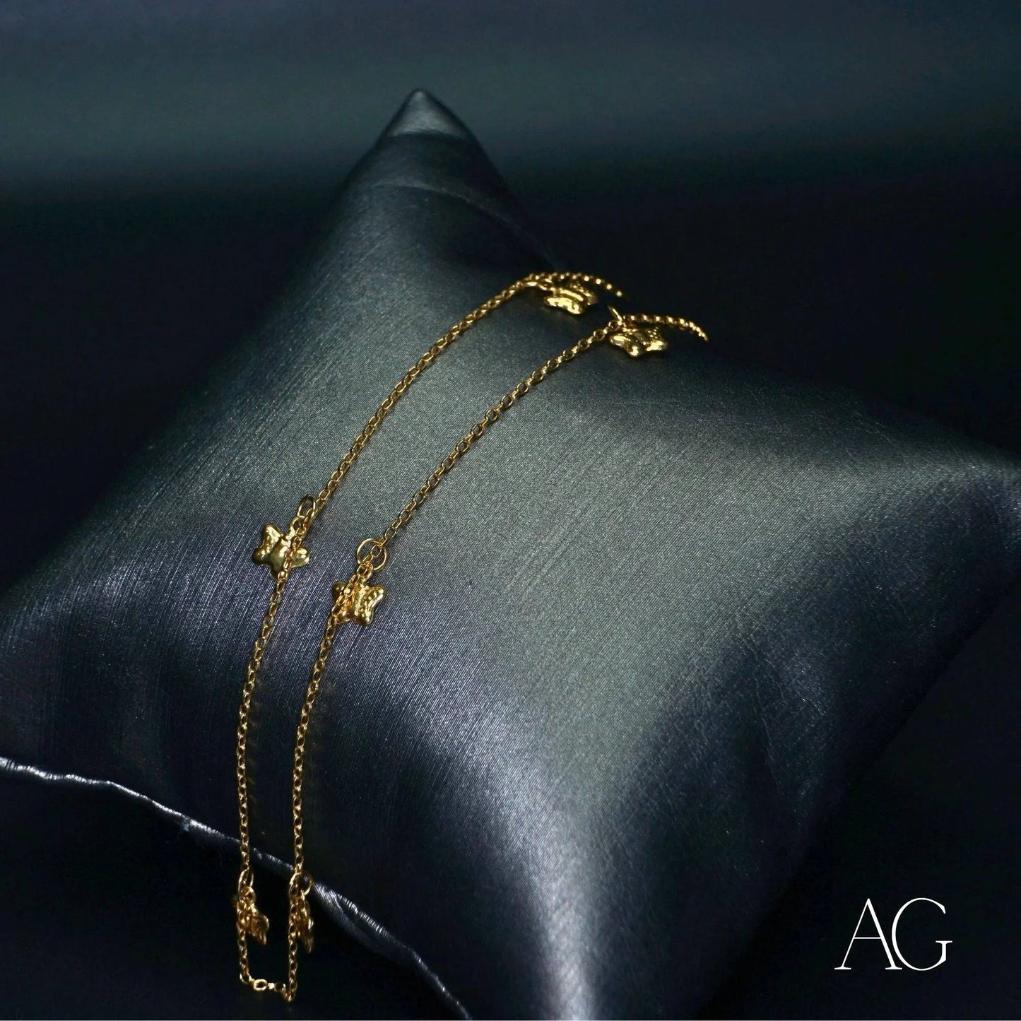 Delicate 18k gold anklet with butterfly charms on a dark satin pillow