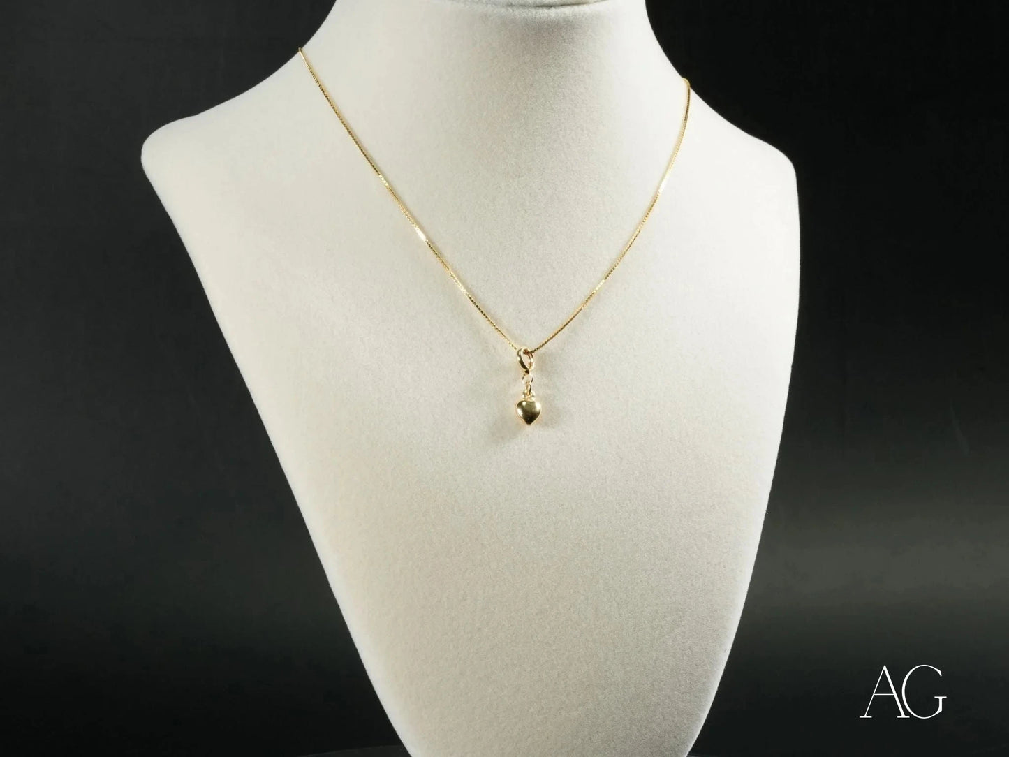 Gold-toned 18k gold necklace featuring a golden heart pendant on a white bust form