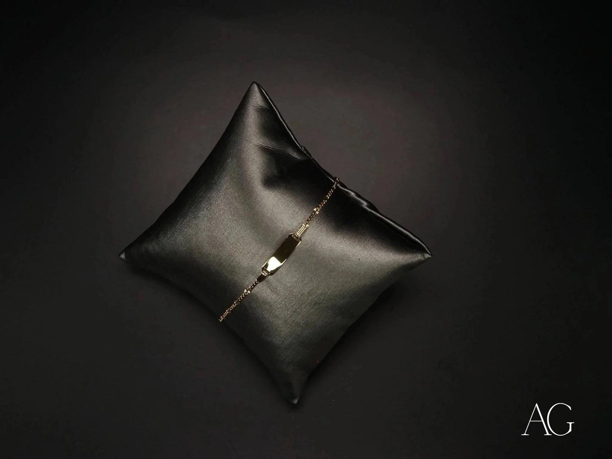 Black leather cushion with diamond tear showcasing 18k gold kid’s ID bracelet with spring ring lock