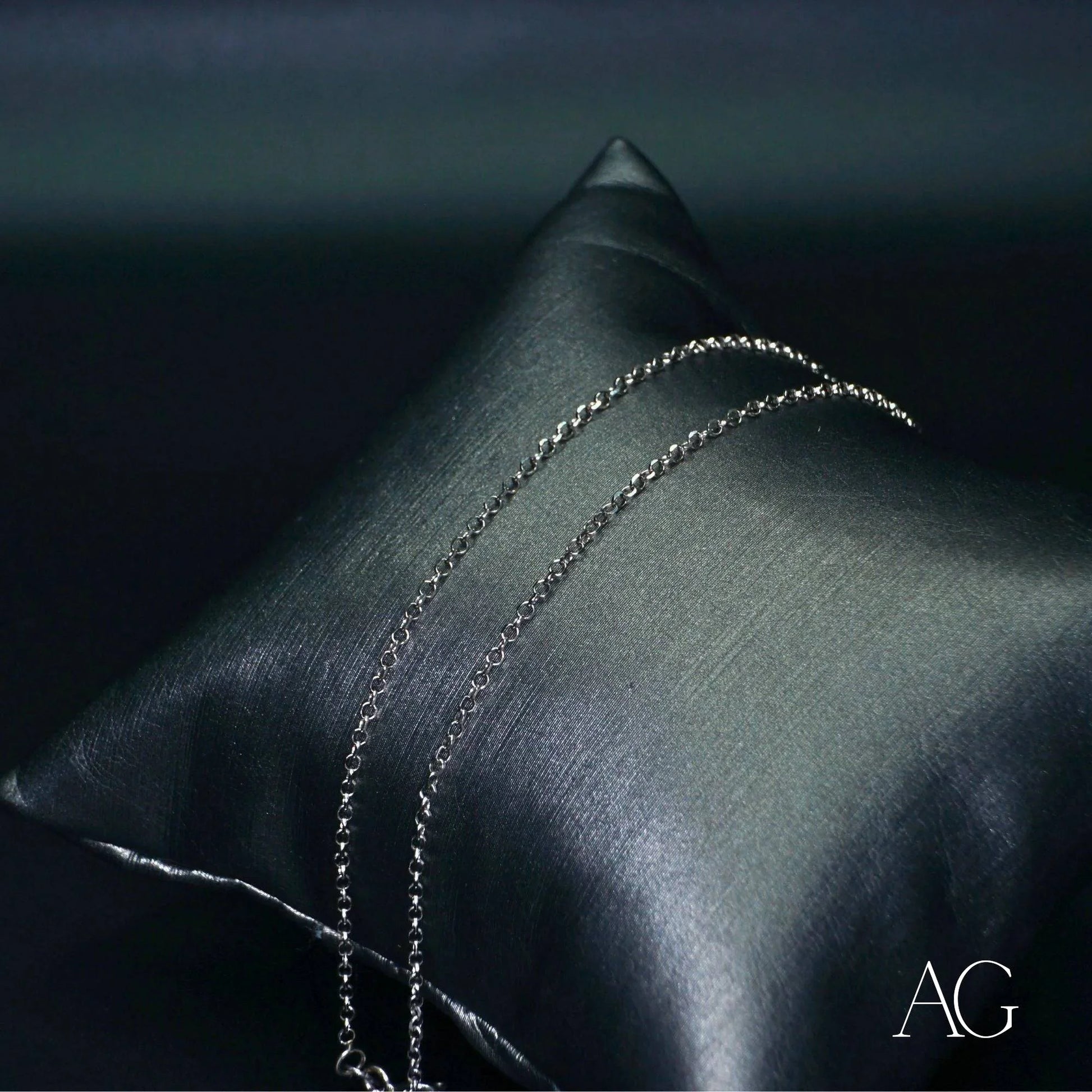 Dark gray satin pillow with an 18k white gold anklet and silver chain elegantly draped