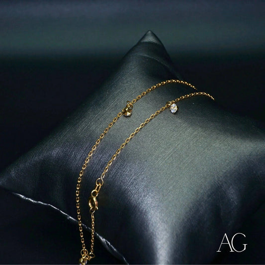 Delicate 18k gold anklet with zirconias displayed on a dark cushion