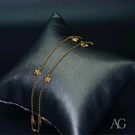 Delicate 18k gold anklet with butterfly charms on a dark satin pillow