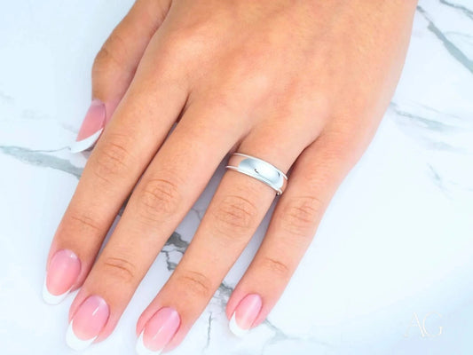 Hand with pink nails wearing a silver ring next to an Elegant White Gold Wedding Band