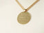 Gold-toned medallion necklace with engraved tudo posso text, part of Golden Faith collection