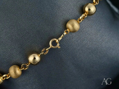 Gold bead bracelet featuring smooth and textured spheres with a spring ring clasp