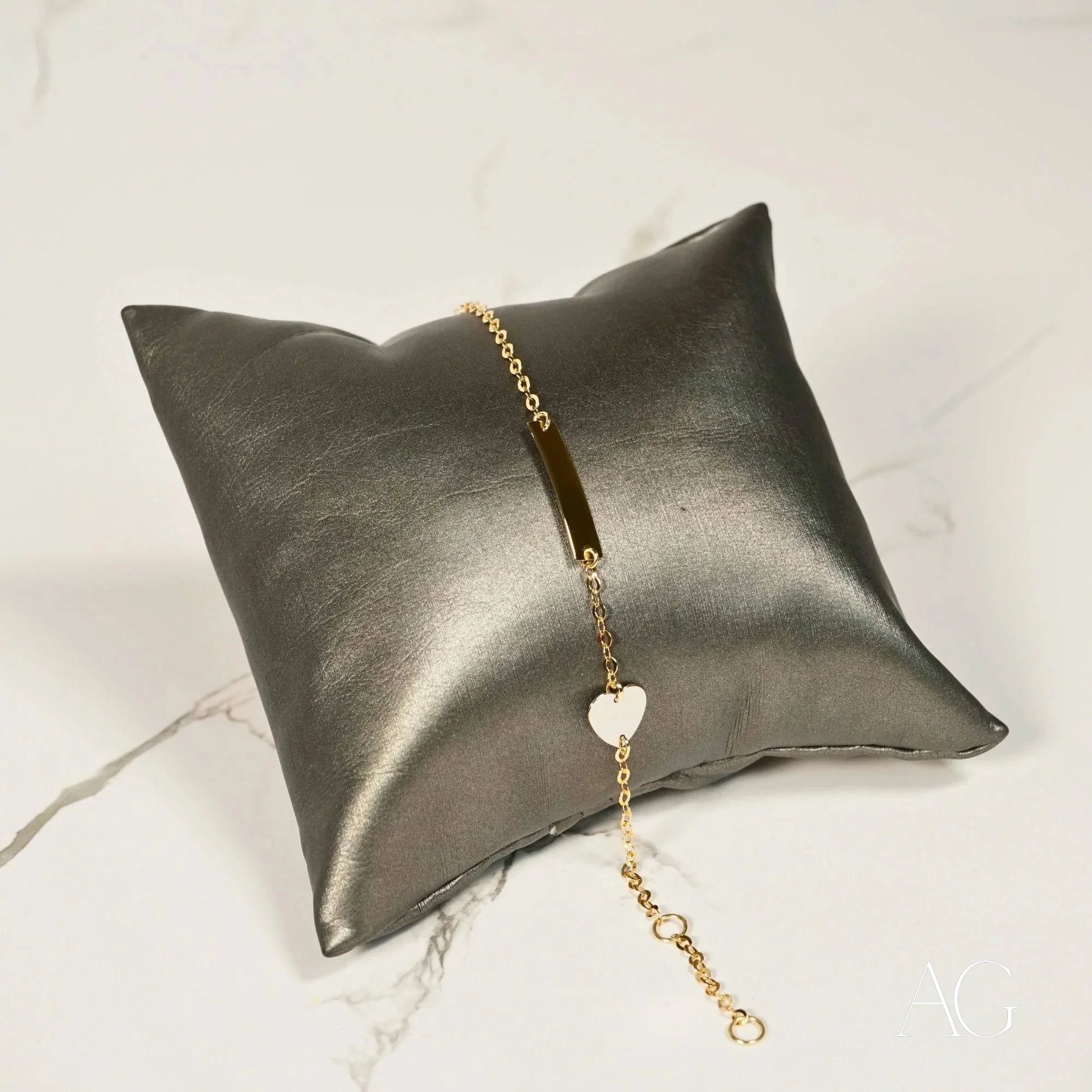 Metallic silver pillow featuring a Children’s ID bracelet in yellow gold with white gold heart motif