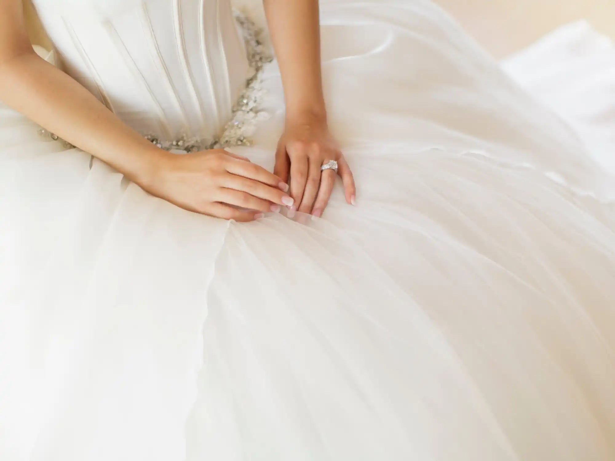 Delicate white wedding dress with folded hands resting on its fabric.