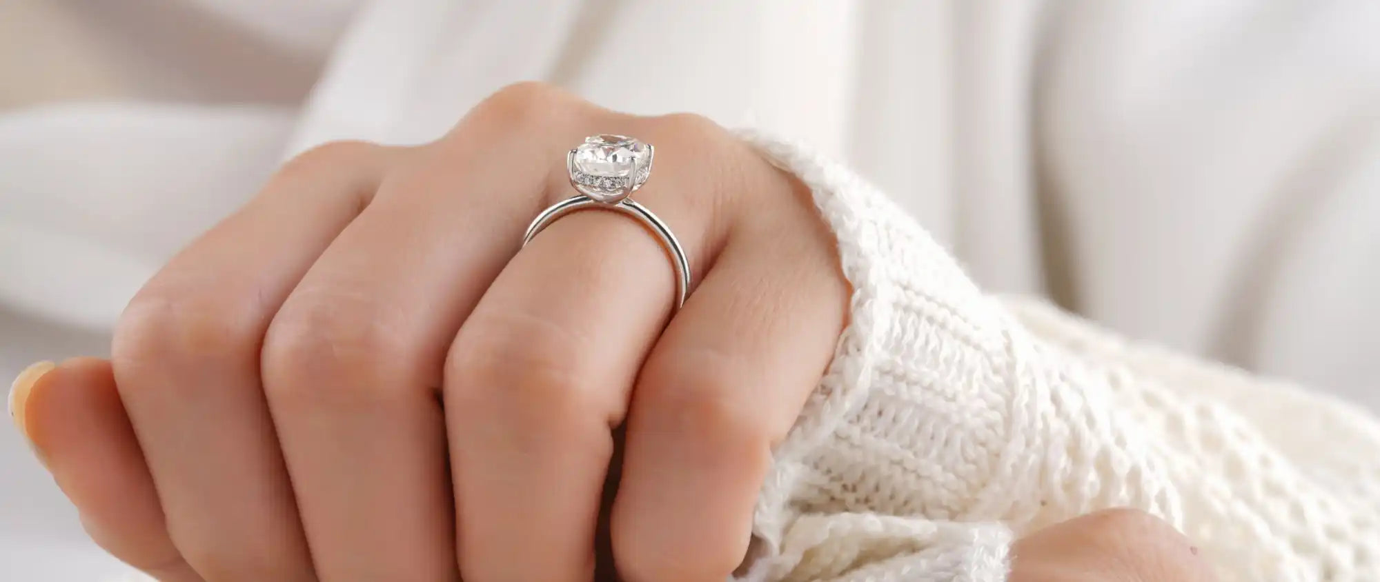 Sparkling diamond engagement ring worn on a hand in a white sweater.