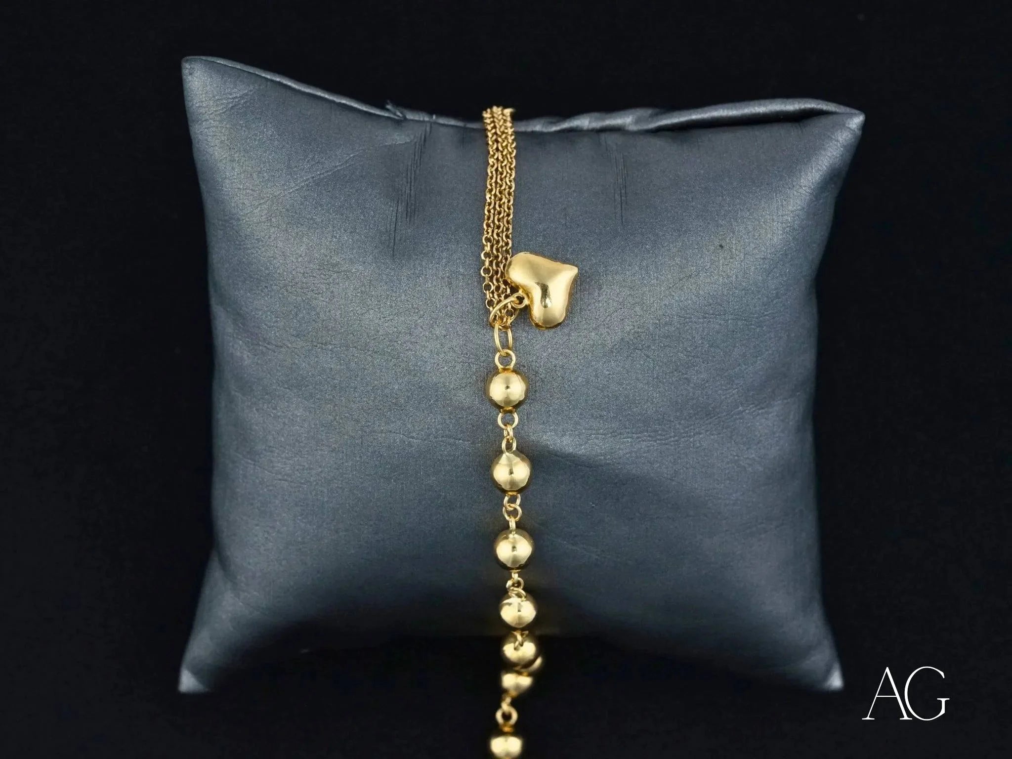 Gold necklace with polished gold beads and heart motif charm on dark cushion