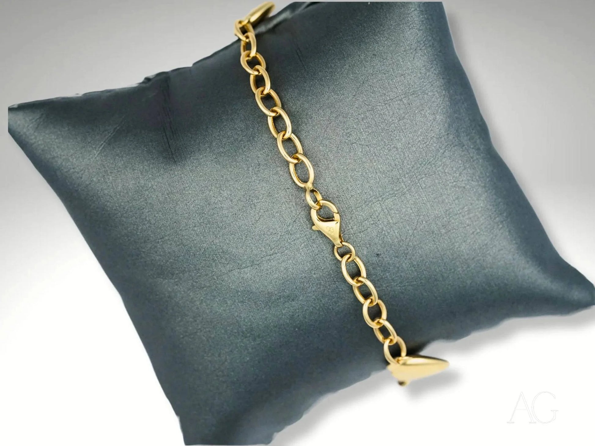 Elegant 18k gold bracelet with heart motifs on a dark gray cushion display