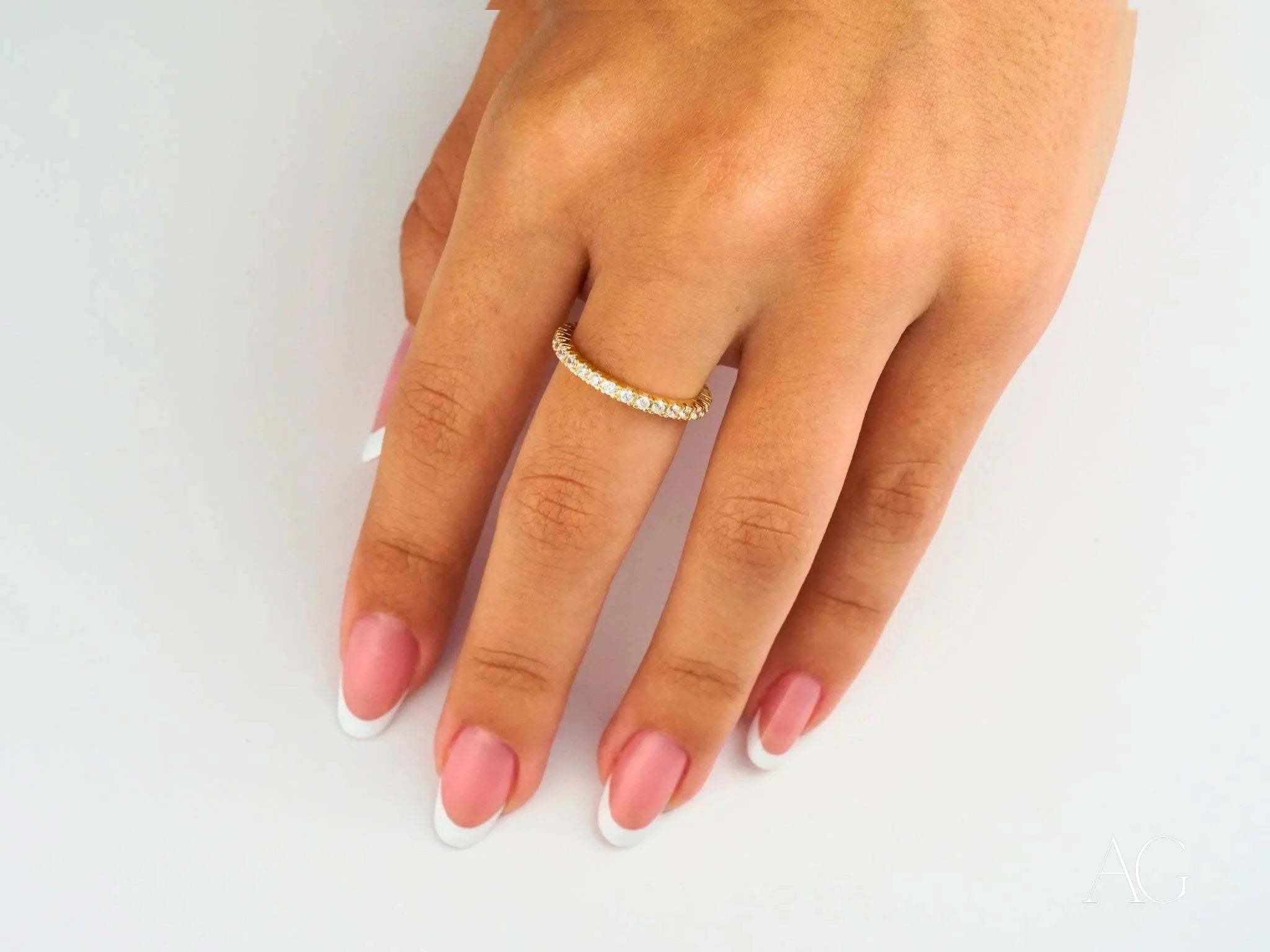 Diamond eternity band on ring finger with pink nails showcasing an elegant 18k gold ring