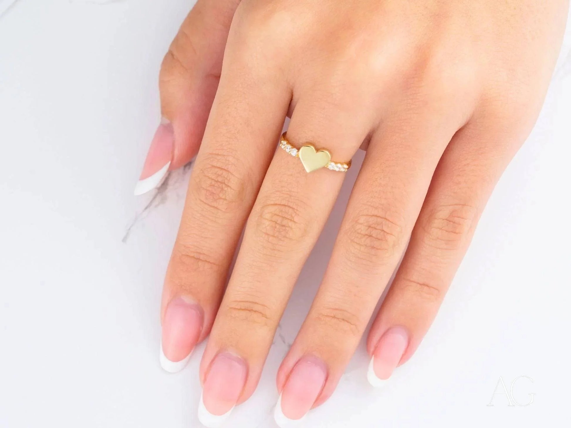 Gold heart-shaped ring on pink manicured nails, showcasing elegant 18k yellow gold design