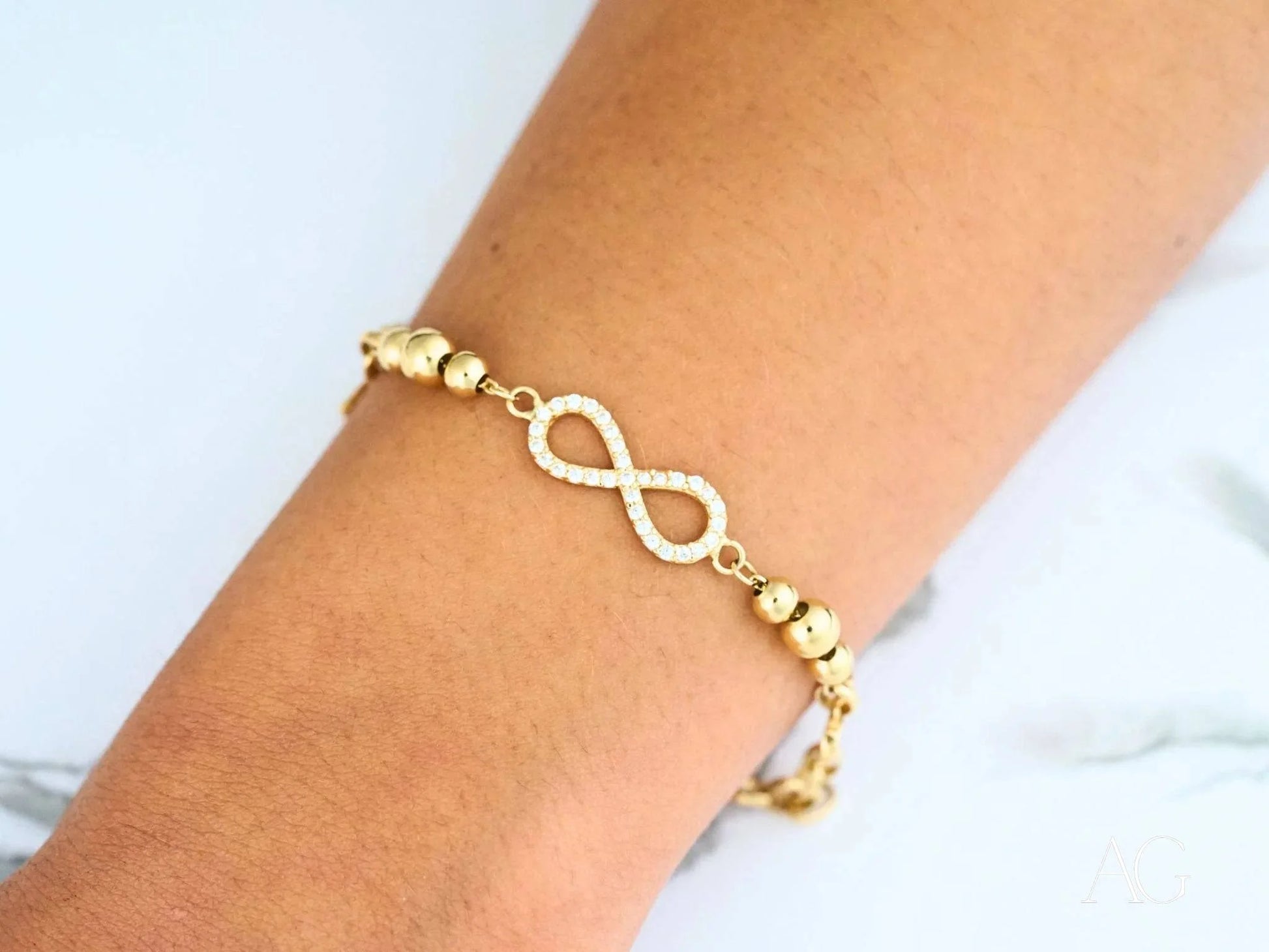 Gold-toned infinity symbol bracelet with beaded accents and sparkling cubic zirconia in 18k gold