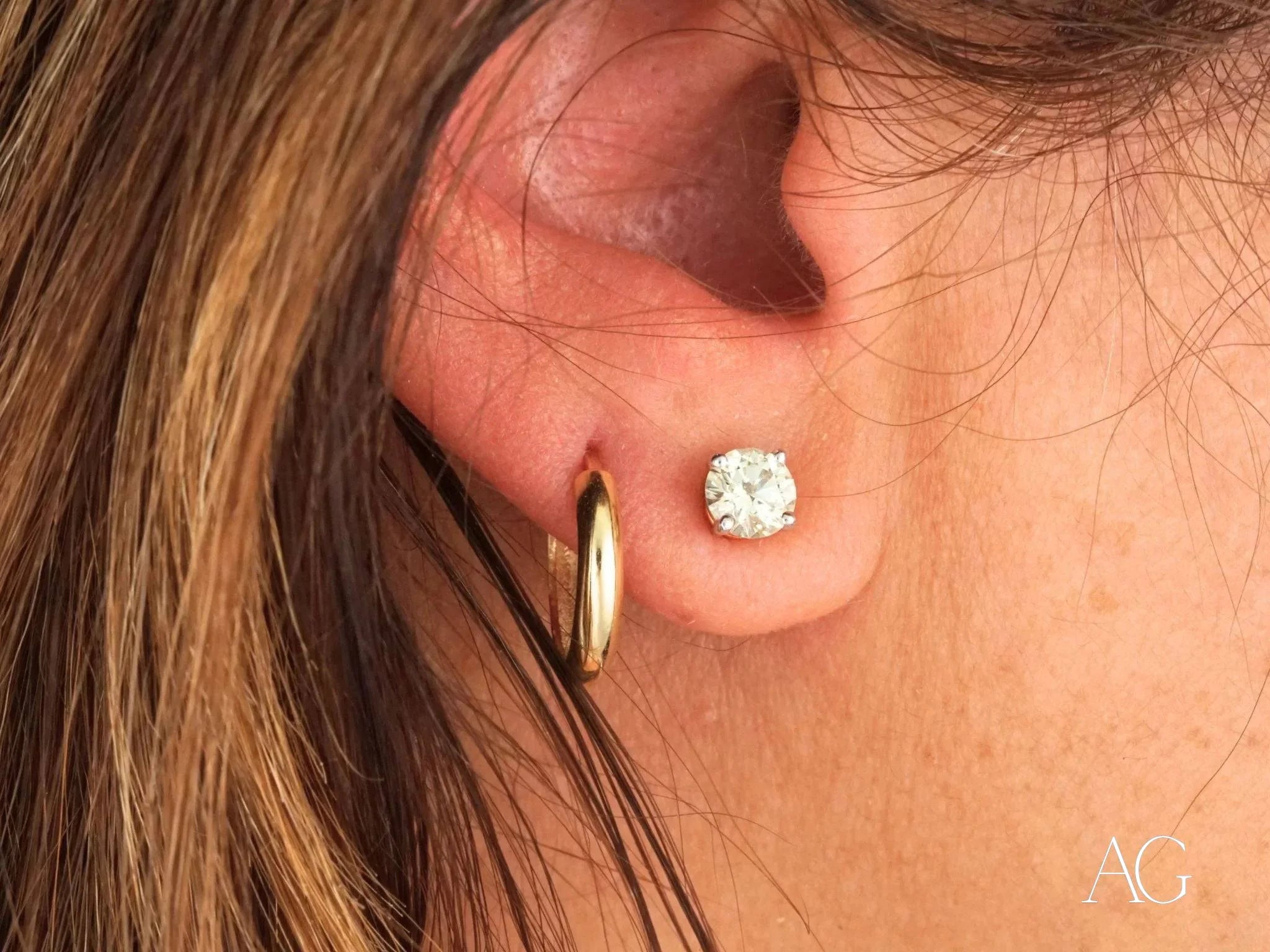 Diamond stud earring in pierced earlobe with 18k yellow gold mini hoops earrings