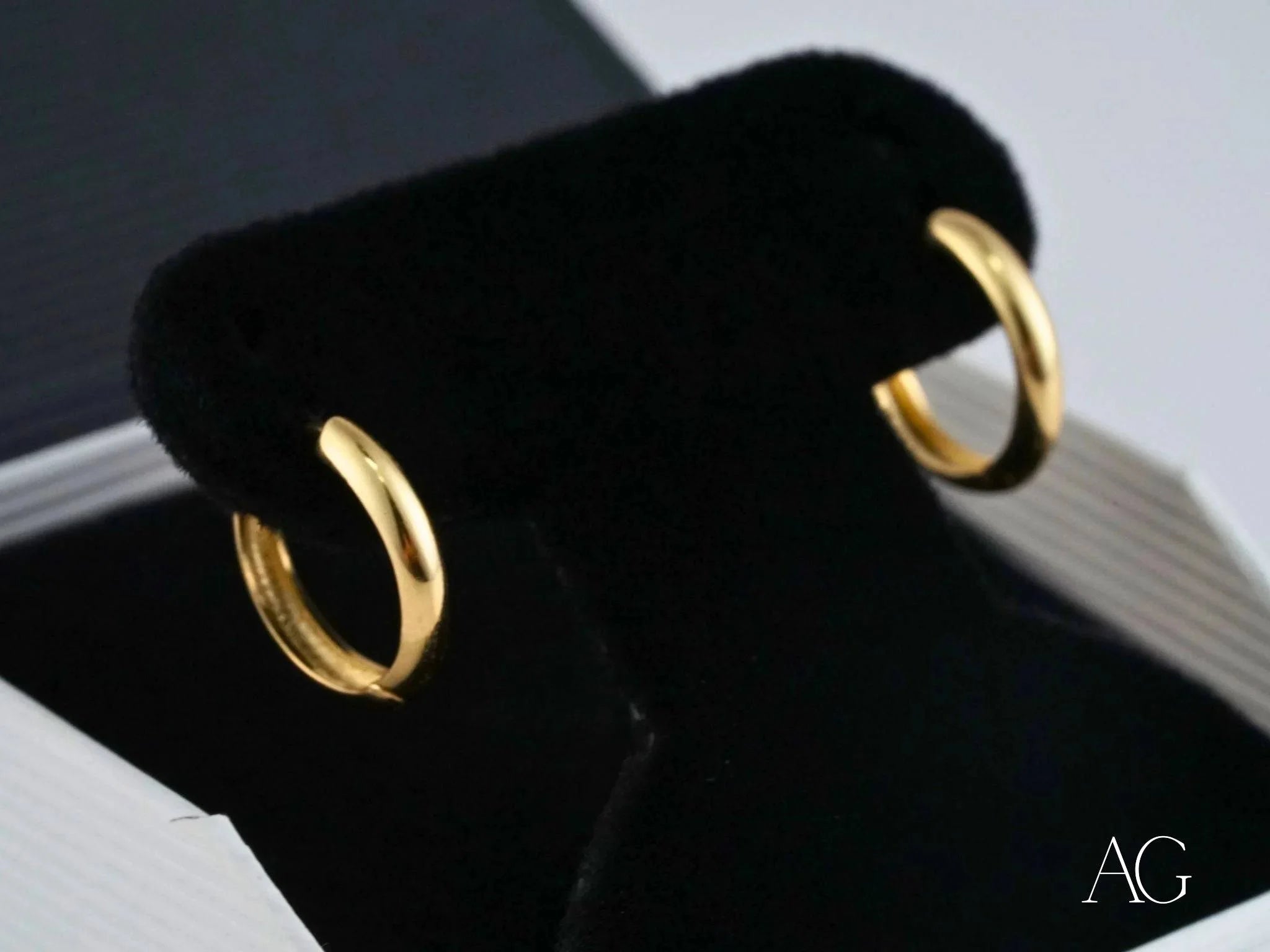 Gold hoop earrings on a black velvet stand showcasing 18k yellow gold elegance