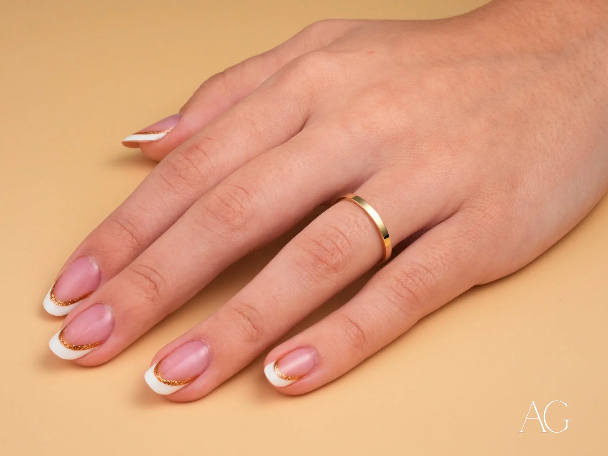 Hand wearing minimalistic 18k gold wedding band from Essence Collection with French manicure