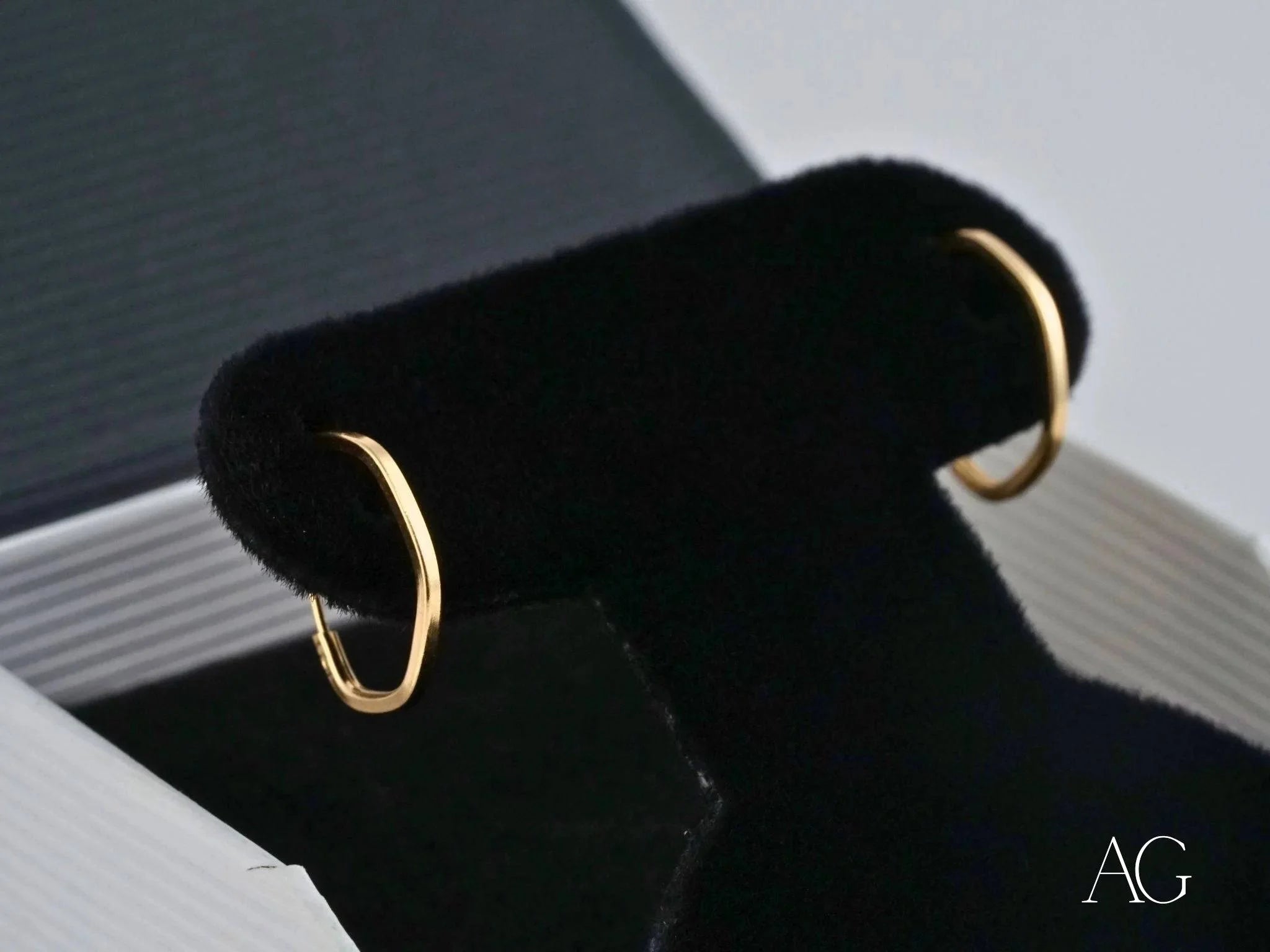 Gold hoop earrings on a black jewelry stand showcasing Glimmergold 18k mini design