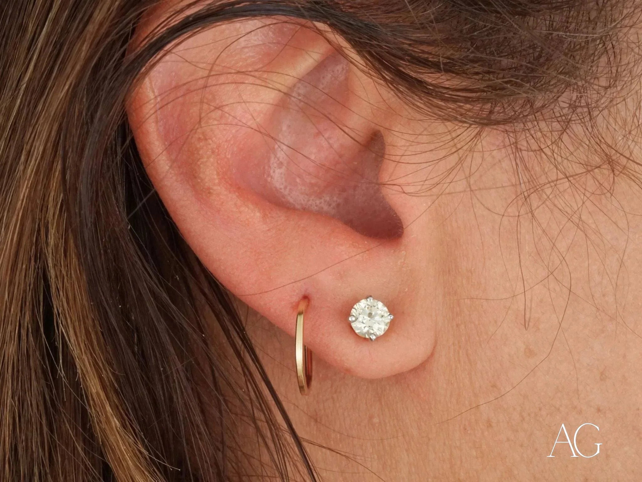 Human ear adorned with Glimmergold 18k mini hoops and a diamond stud earring