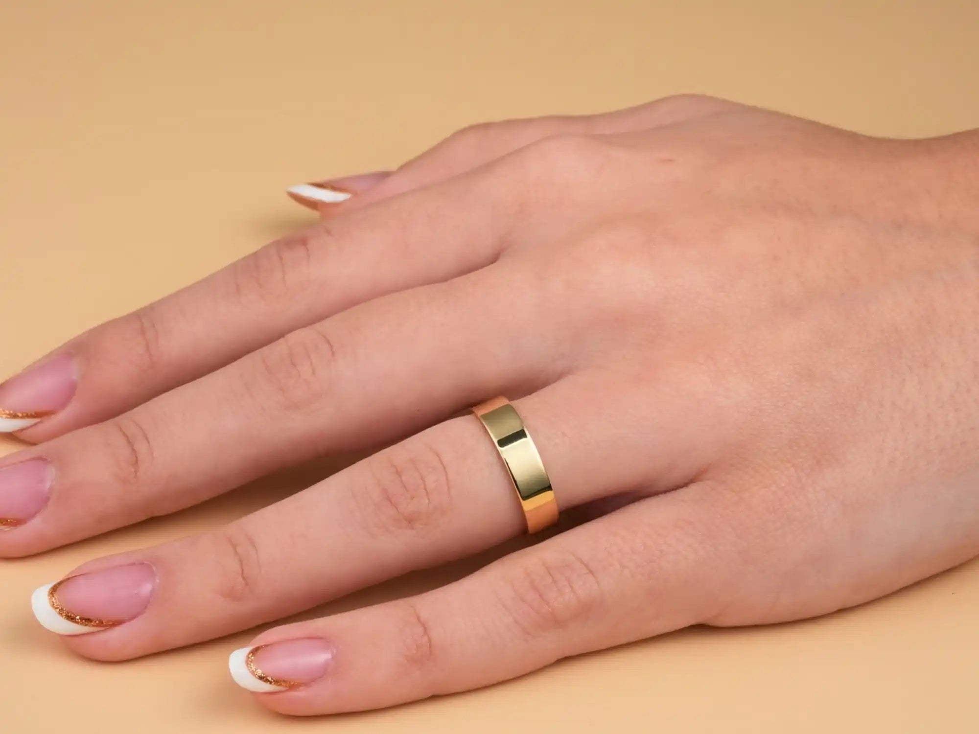 Gold wedding band on a hand with French manicured nails.