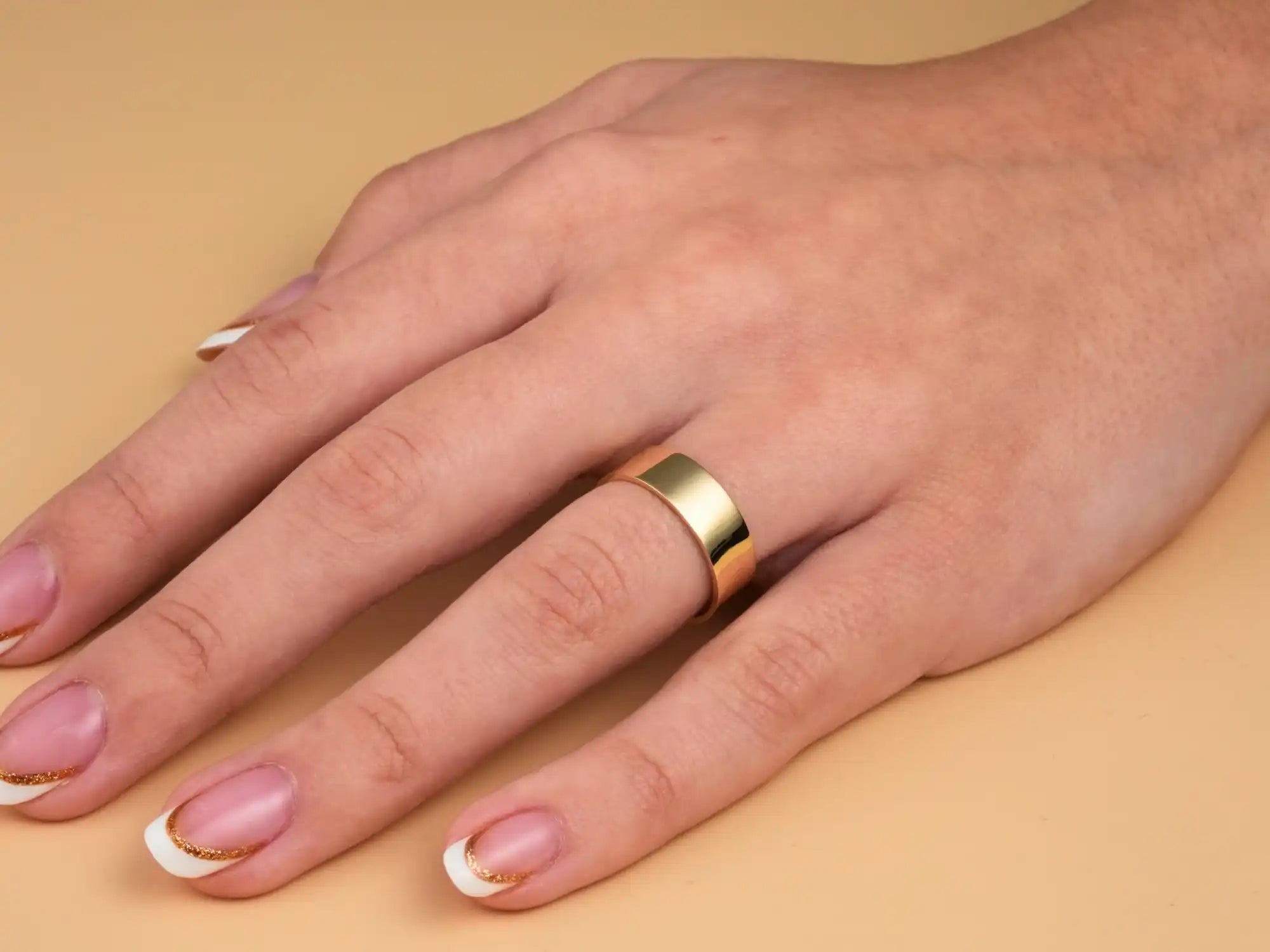 Gold wedding band on a hand with French manicured nails.