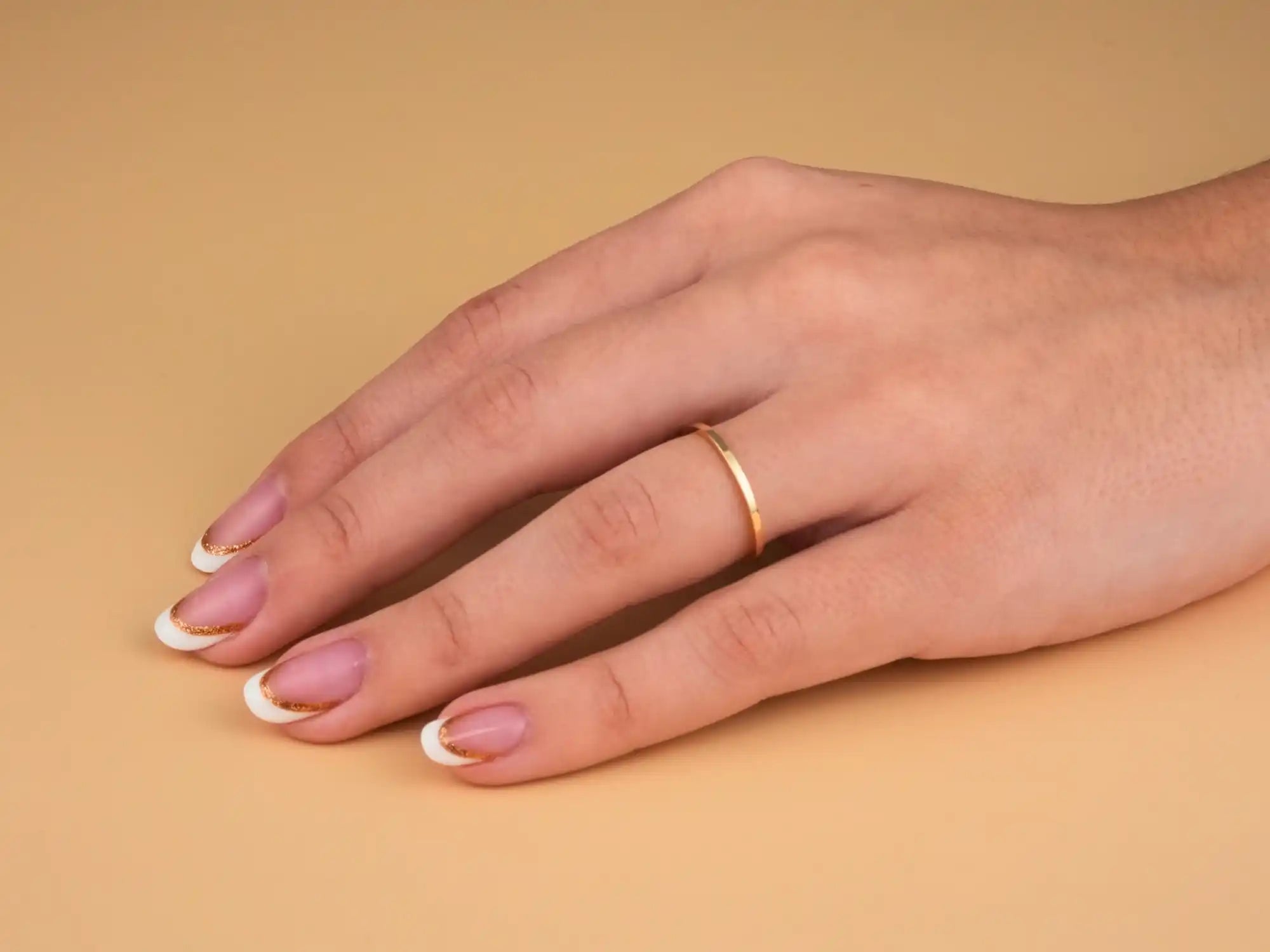 Gold wedding band on a hand with French manicured nails.