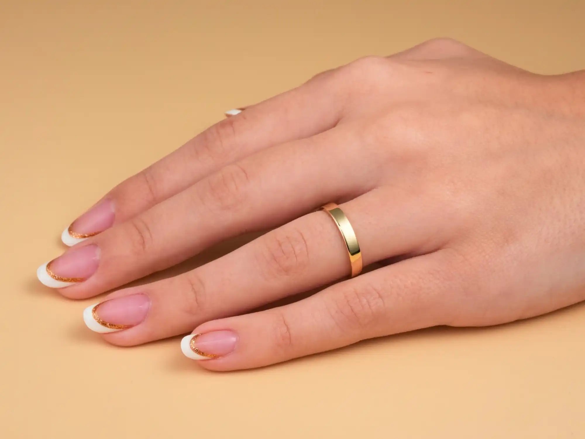 Gold wedding band on a hand with pink manicured nails.