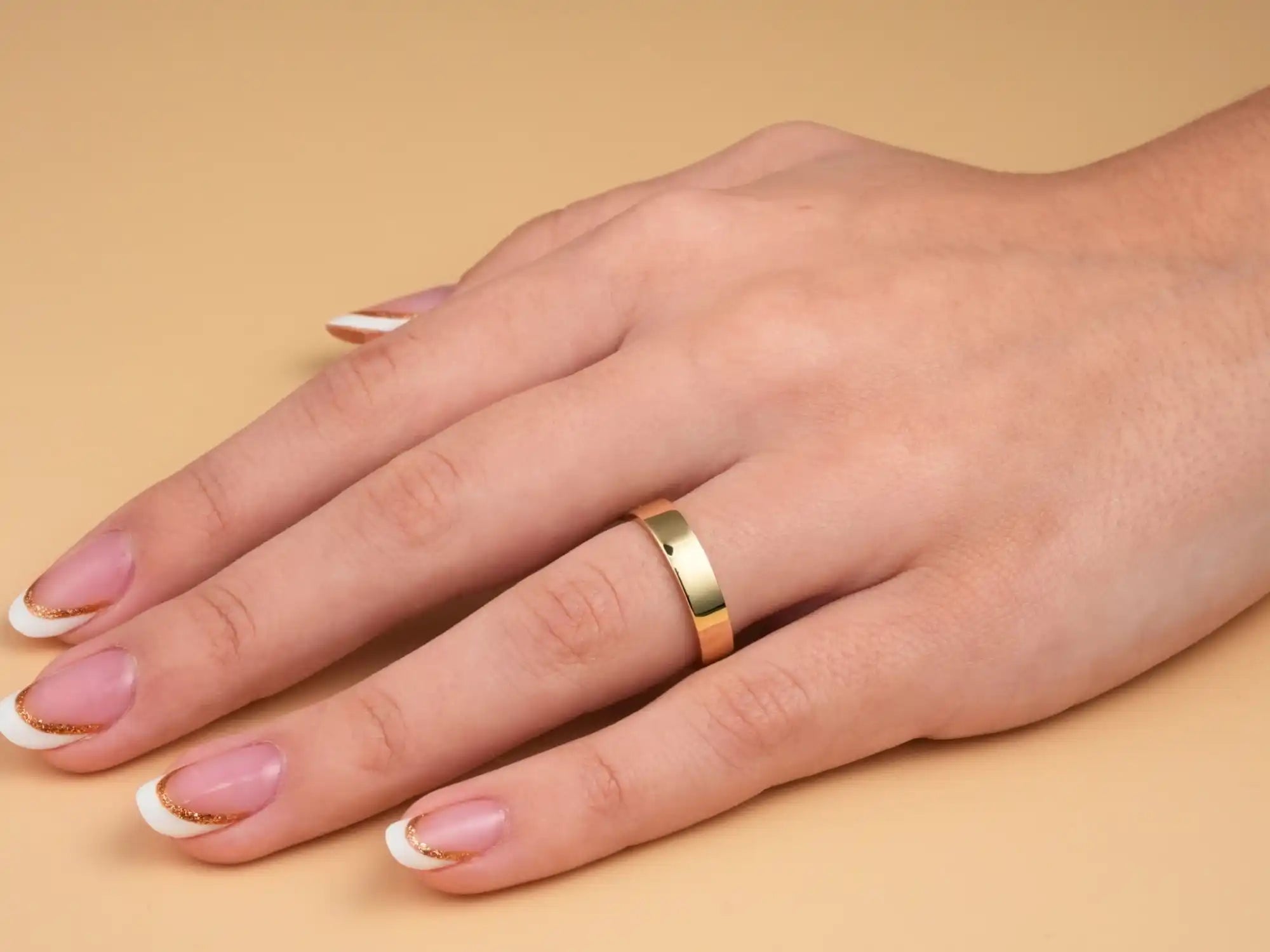 Gold wedding band worn on a hand with French manicured nails.