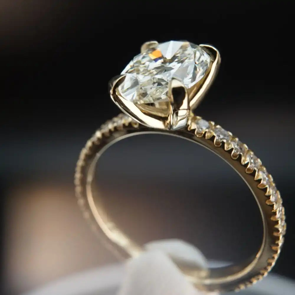 Gold engagement ring featuring a round diamond solitaire with pavé diamonds along the band.