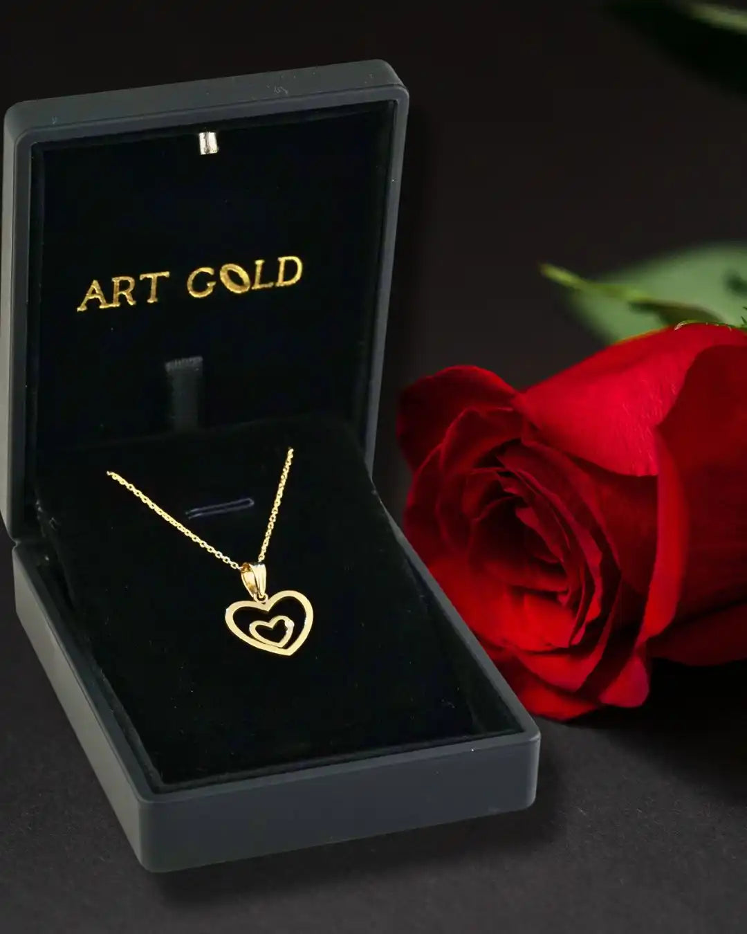 Gold heart-shaped pendant necklace in a black jewelry box alongside a red rose.