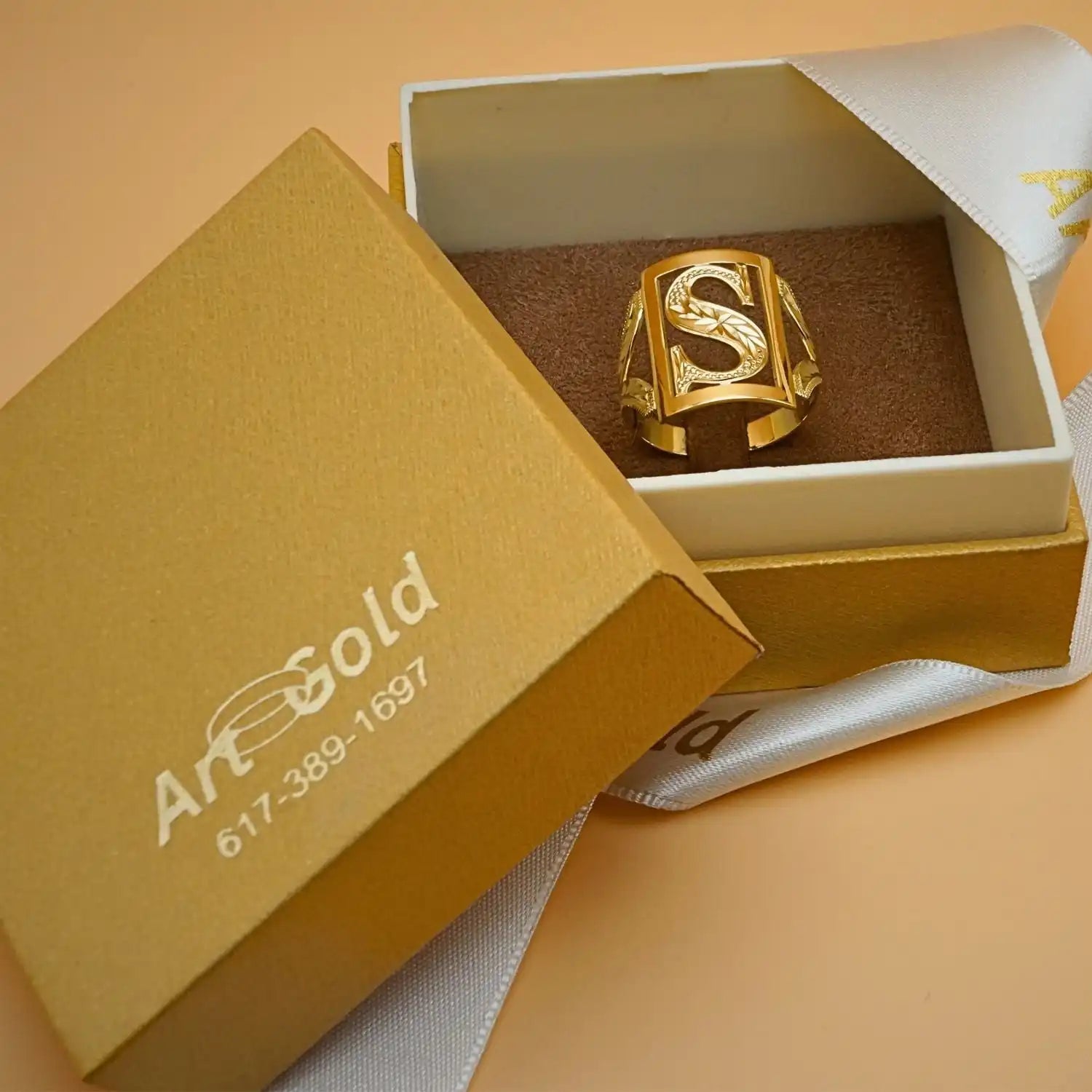 Gold ring with an ’S’ design in a jewelry box.