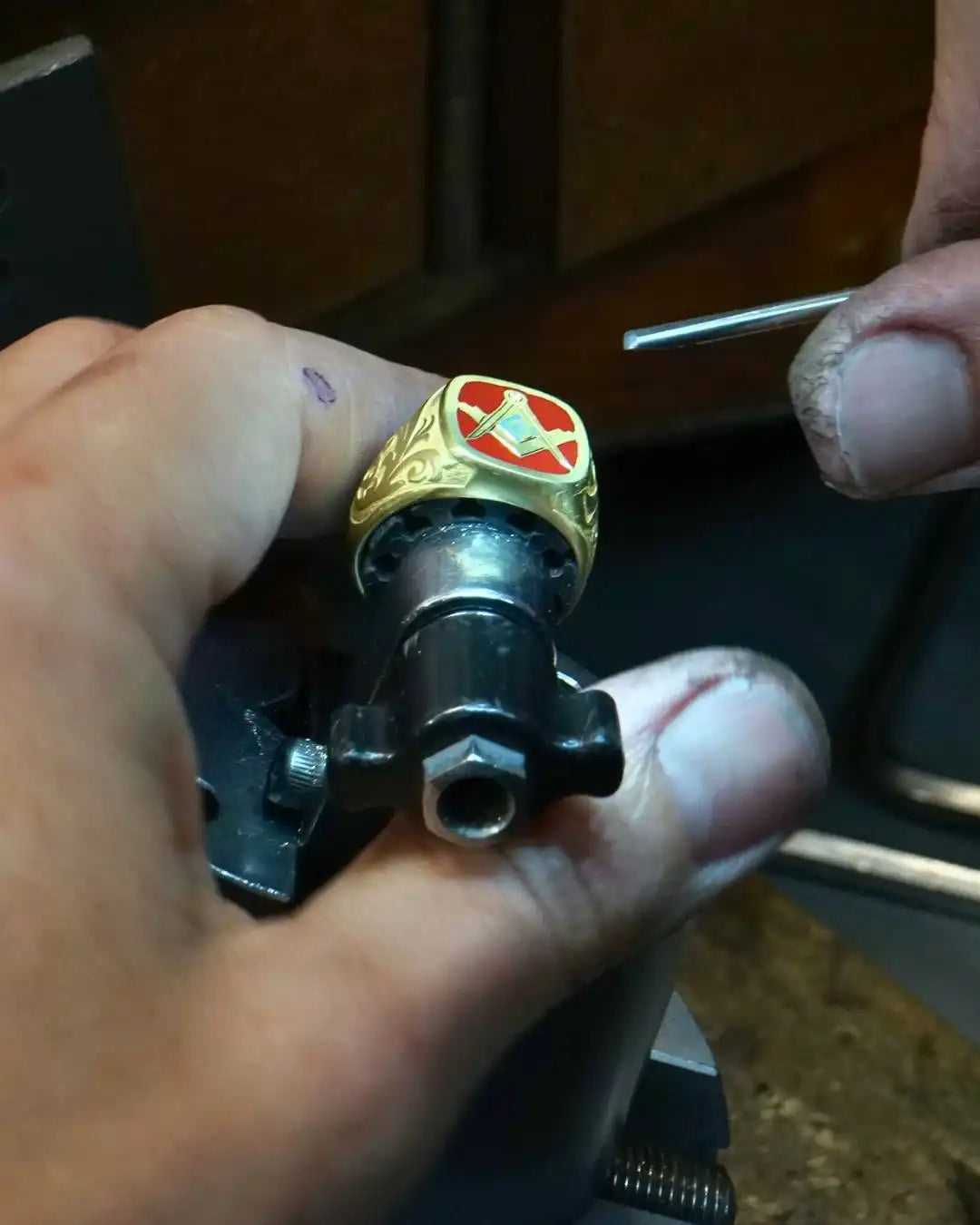 Gold ring with a red cross emblem mounted on a black metal component.