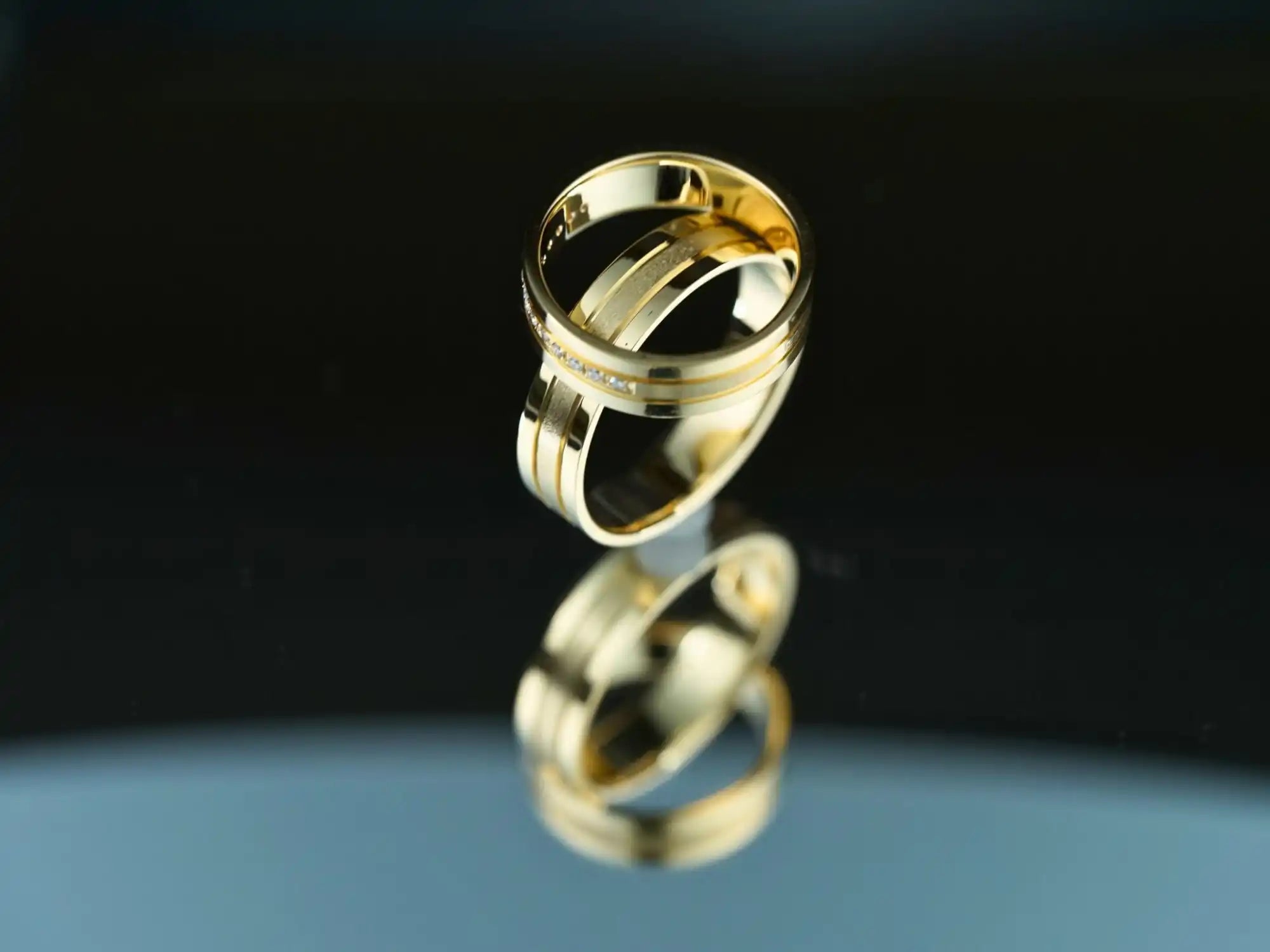 Gold wedding ring with its reflection on a mirrored surface.