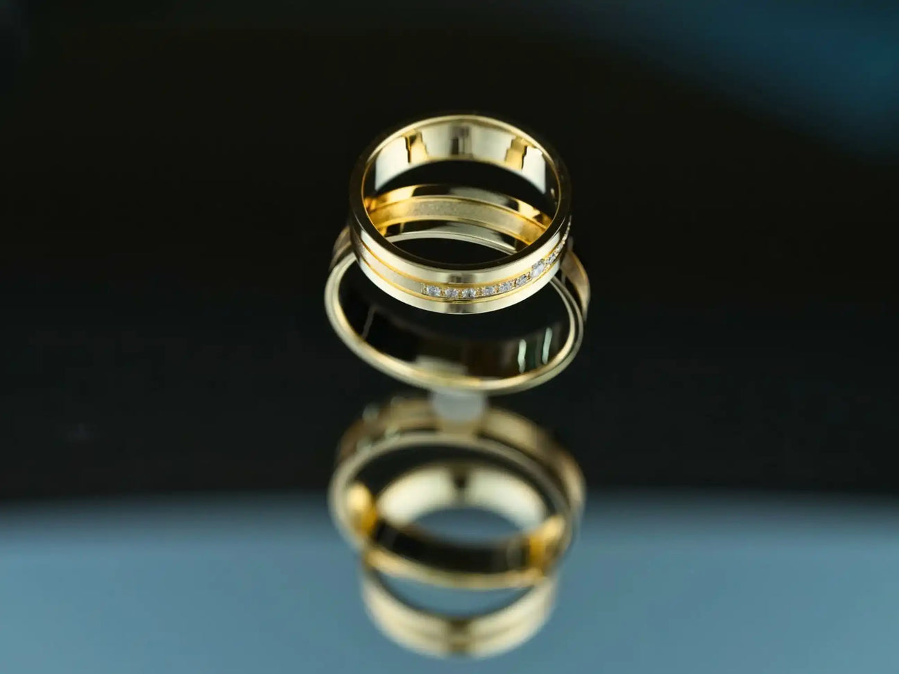 Gold wedding rings with a reflection on a glossy surface.