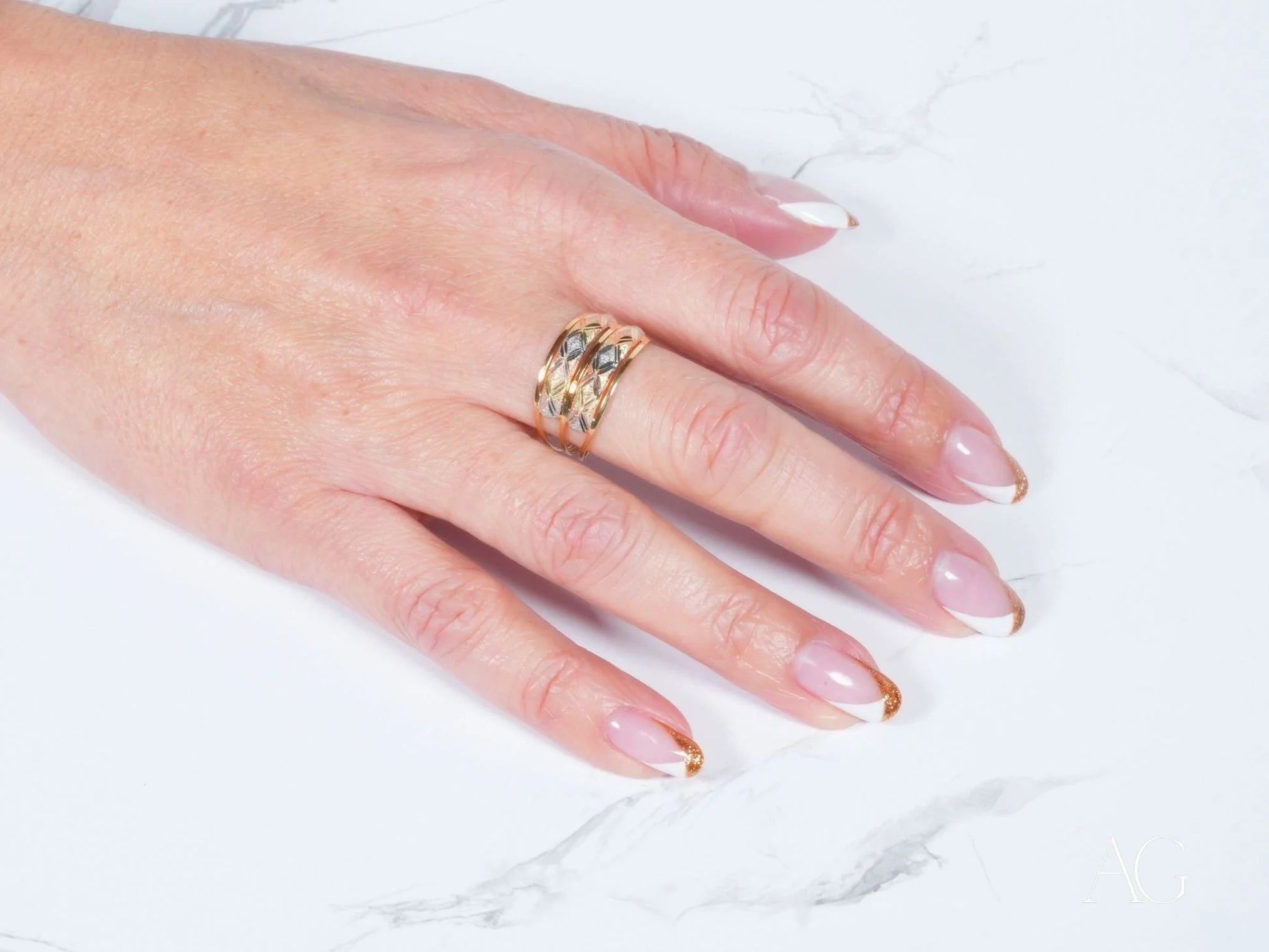 Gold ring with intricate openwork design on manicured hand, showcasing Golden Spectrum 18k 3-tone ring