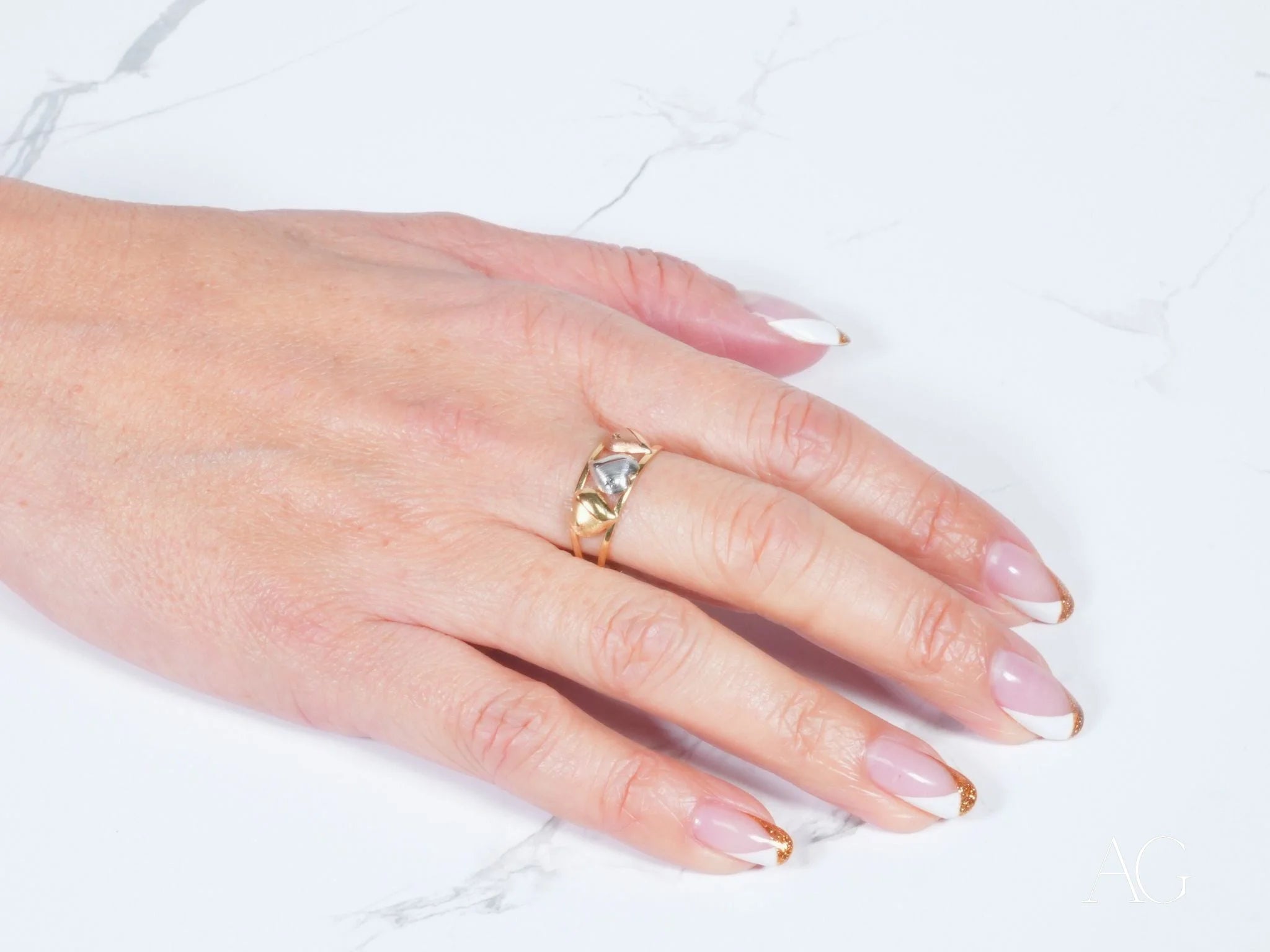 Gold ring with geometric design on a manicured hand from Golden Trio 18k Hearts Ring