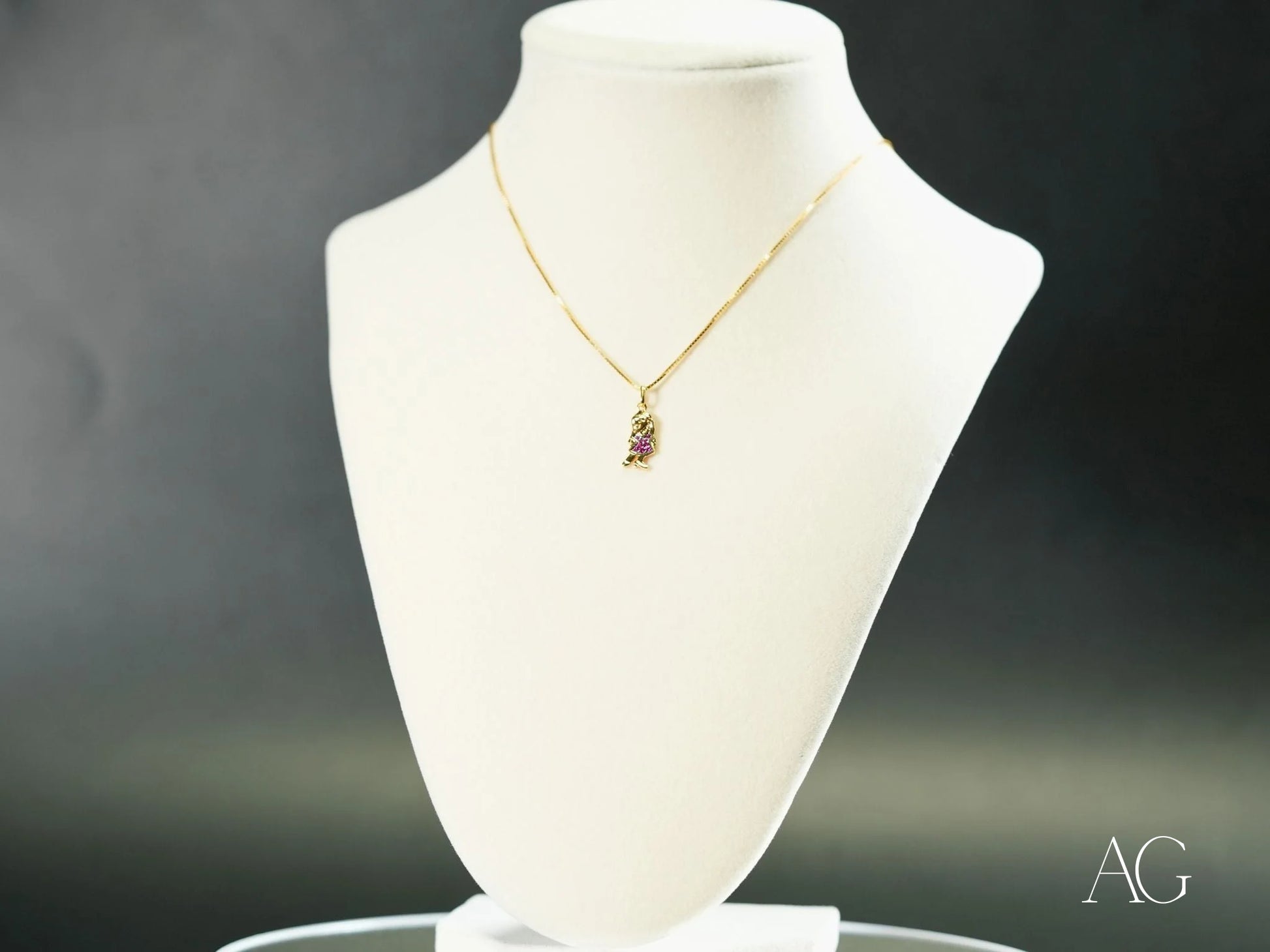 Delicate 18k Gold necklace featuring Golden Ruby Doll pendant on a white bust