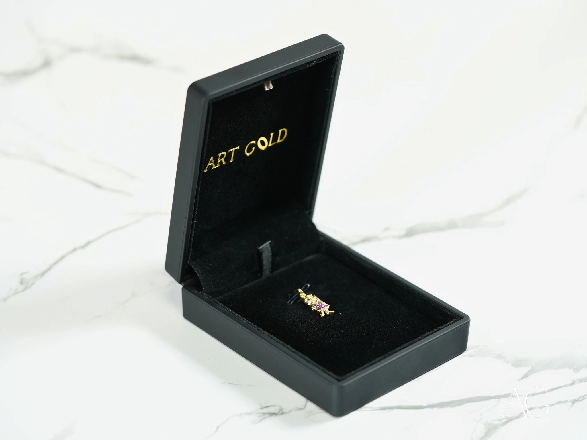 Black jewelry box with ART GOLD text showcasing a gold pin from Golden Ruby Doll pendant