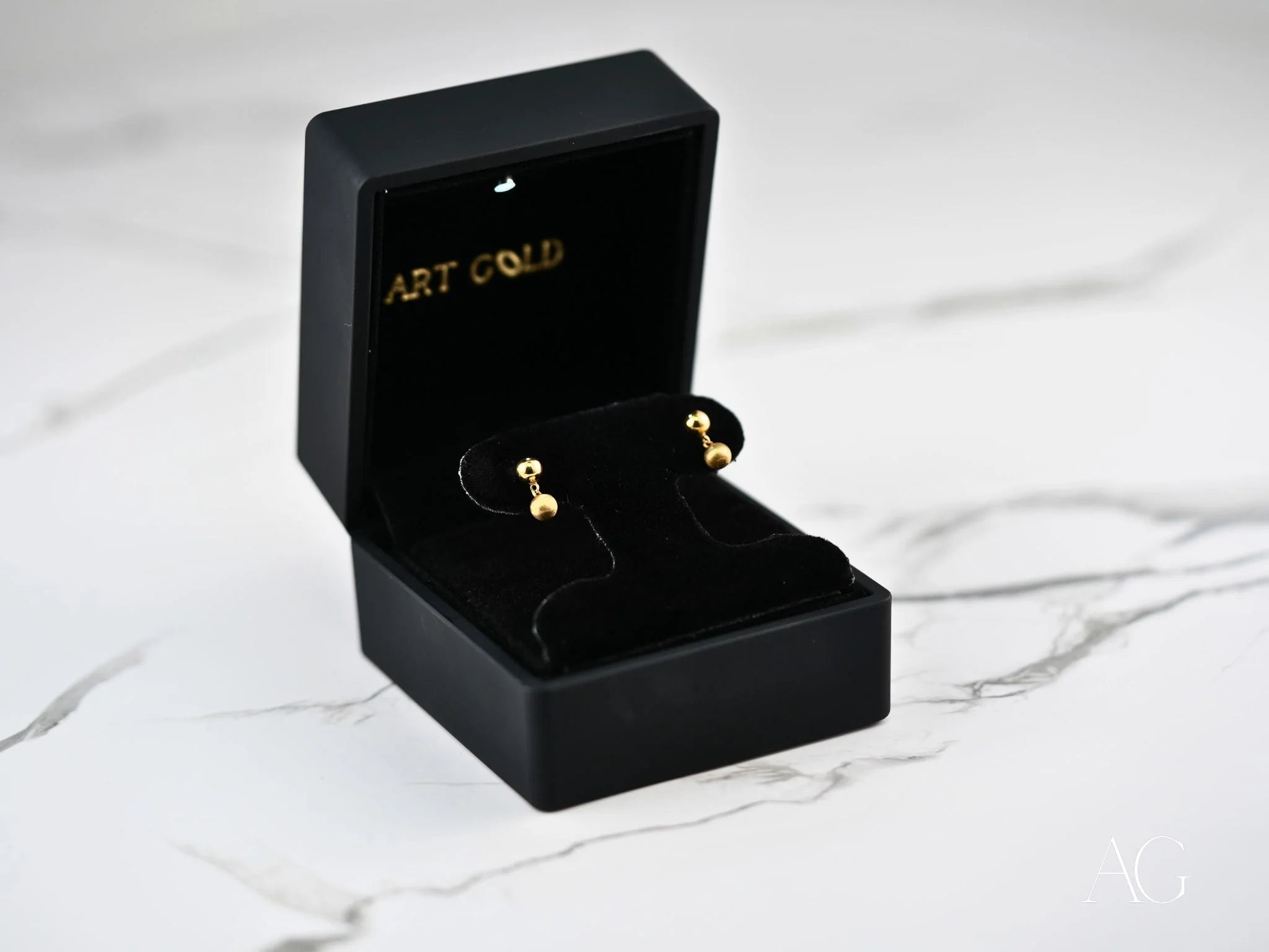 Gold ball earrings in a black jewelry box showcasing 18k gold ball drop design
