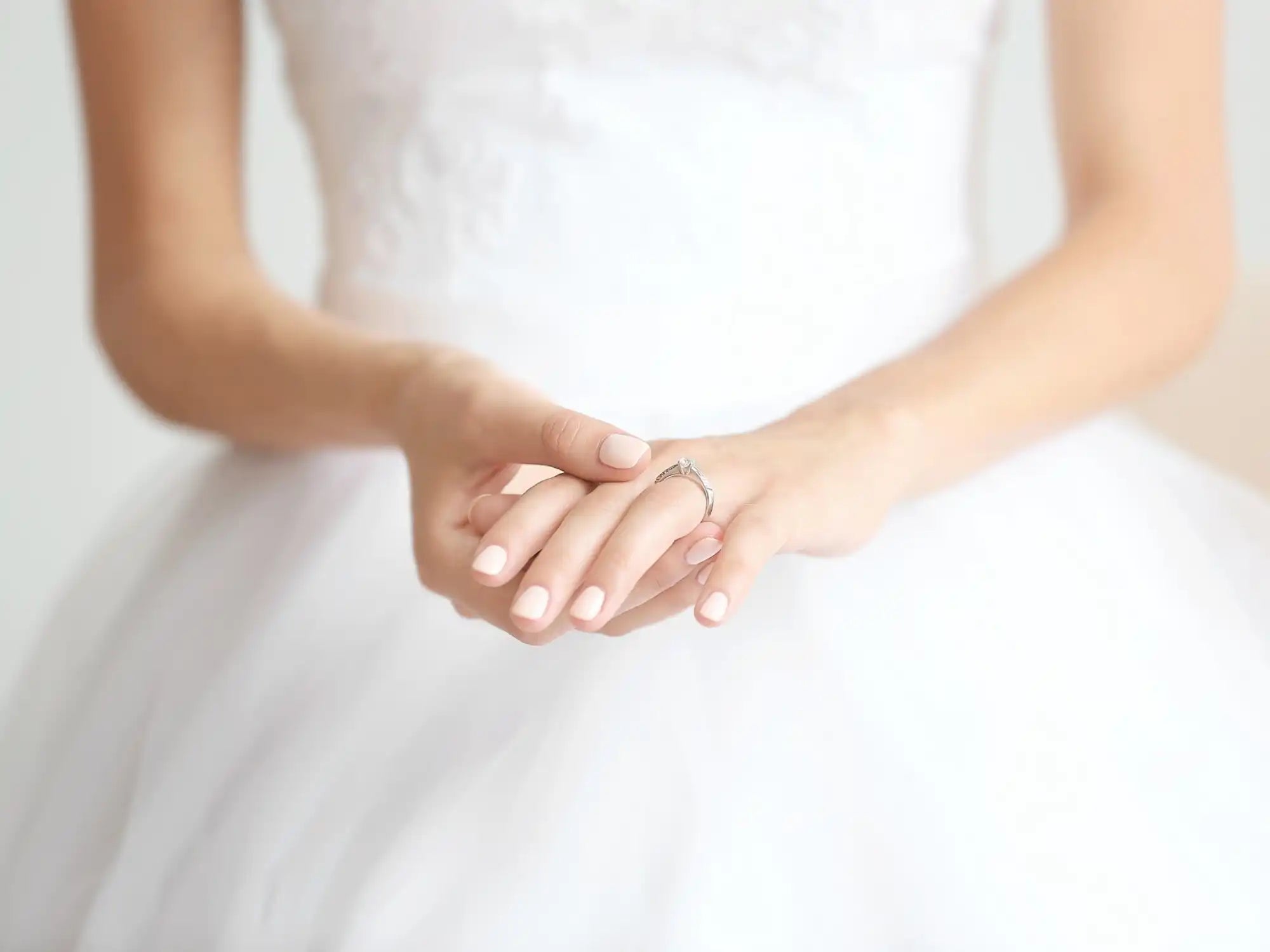 Hands wearing an engagement ring against a white wedding dress.