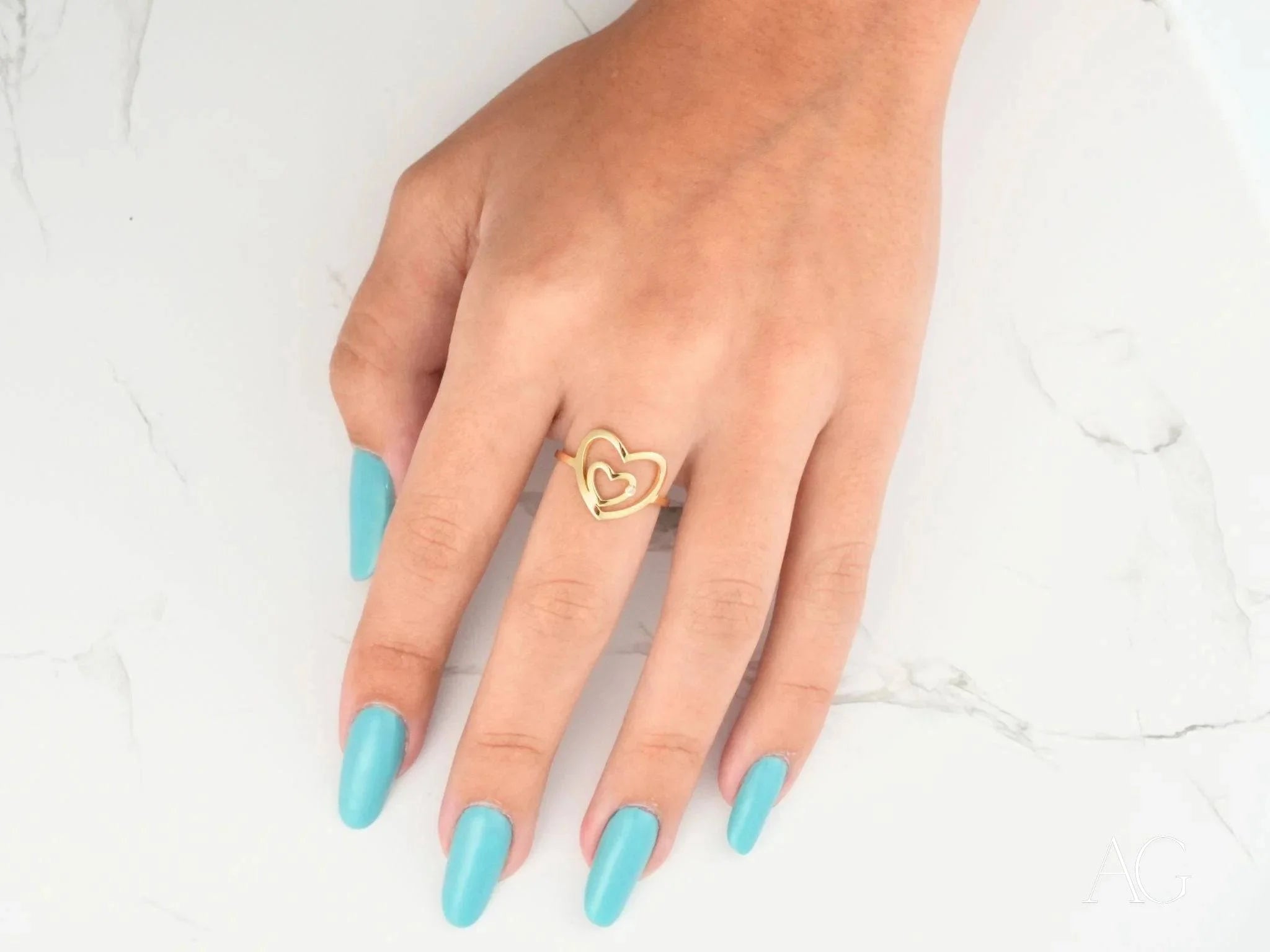 Gold heart ring with diamond in 18k yellow gold worn on a finger with turquoise nails