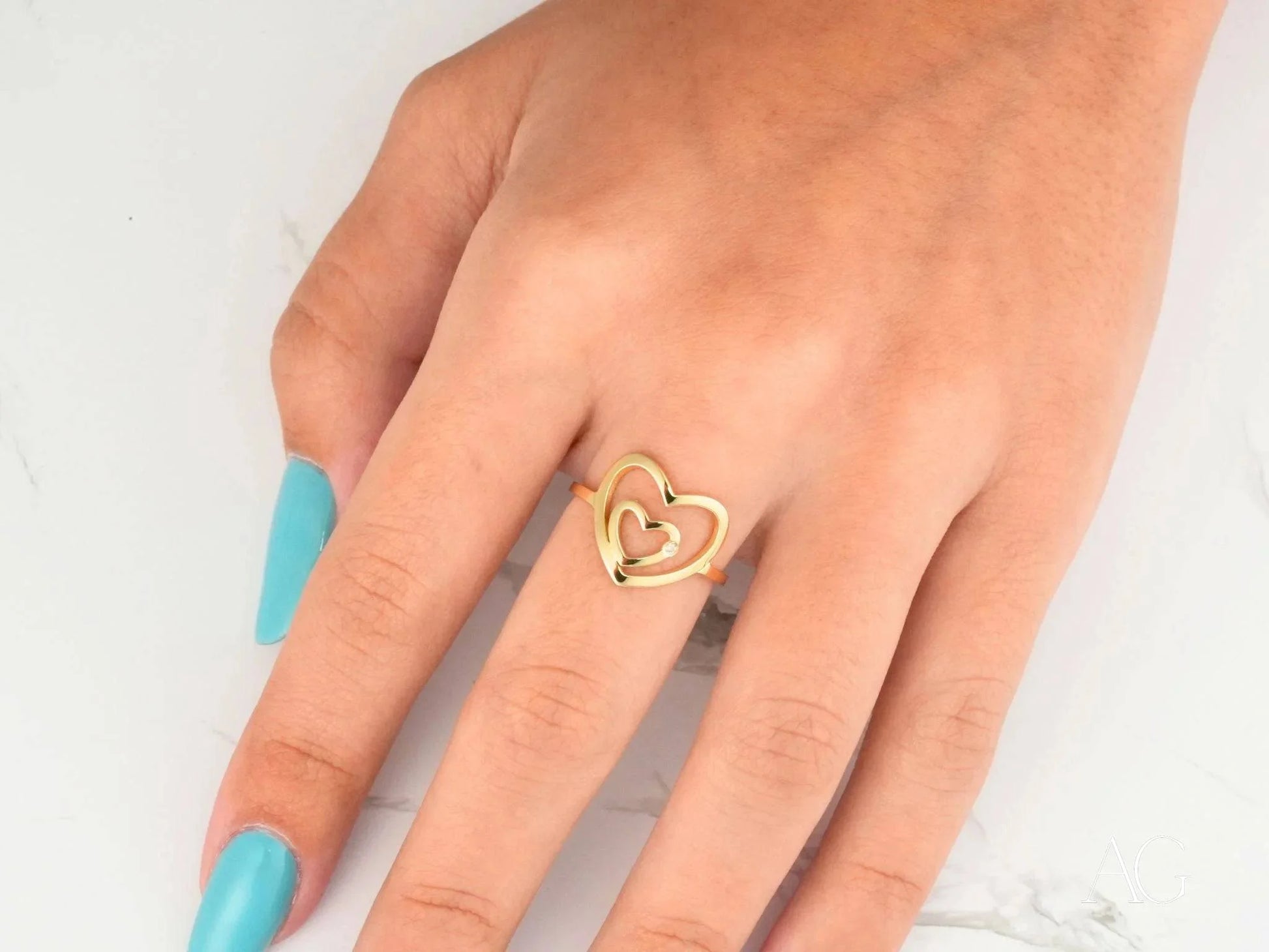 Gold heart ring in 18k yellow gold worn on a finger with turquoise nail polish