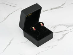 Gold and ruby teddy bear earrings in a black jewelry box beside 18k gold ladybug stud earrings