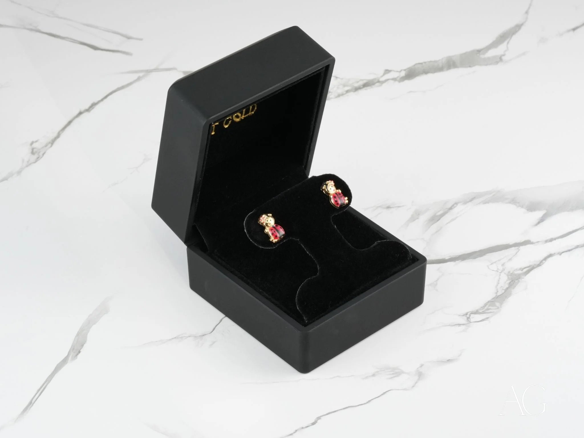 Gold and ruby teddy bear earrings in a black jewelry box beside 18k gold ladybug stud earrings
