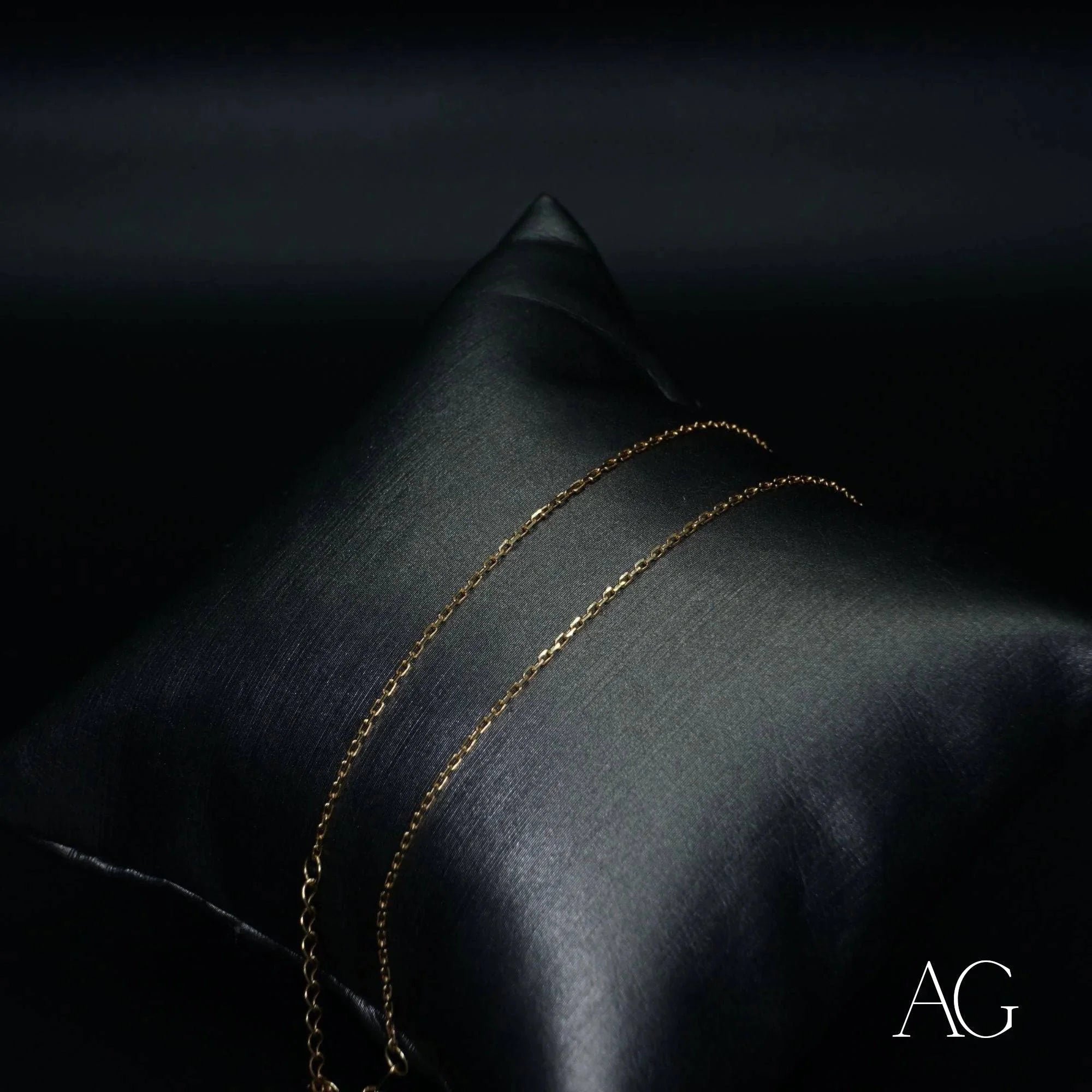 Delicate 18k gold anklet elegantly draped on a dark cushion for luxurious display