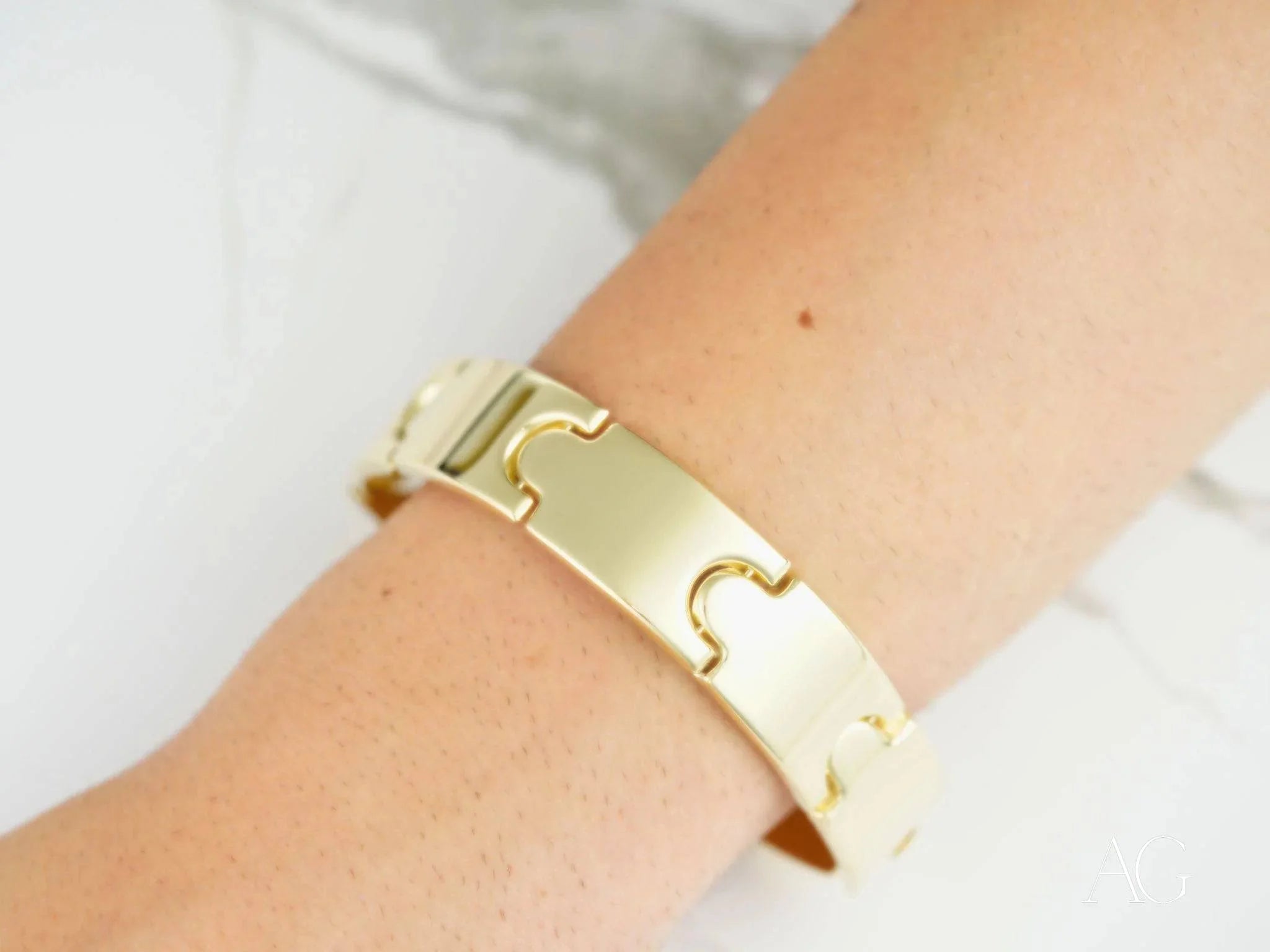 Gold-colored puzzle piece bracelet with open box clasp worn elegantly on a wrist