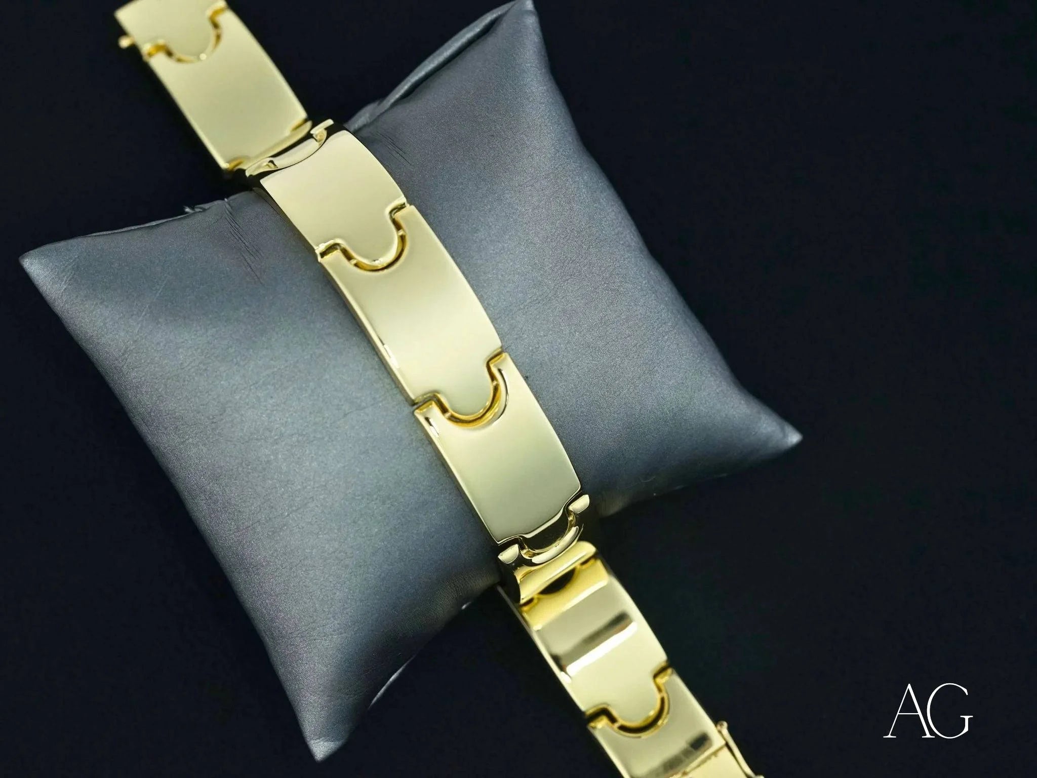 Gold-toned metal bracelet with geometric links and open box clasp on gray cushion