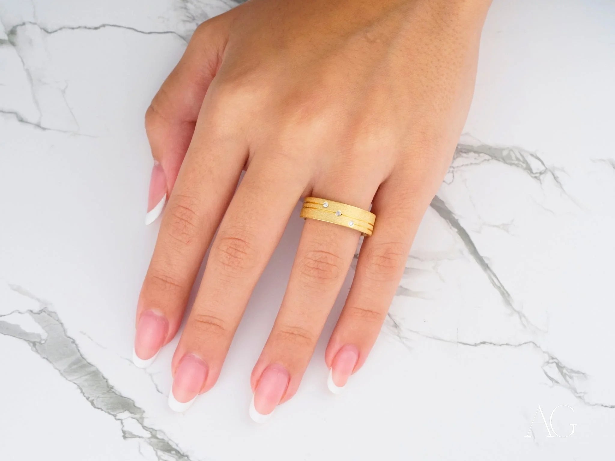 Gold wedding band with diamond accents on a person’s ring finger from Orbit Lines