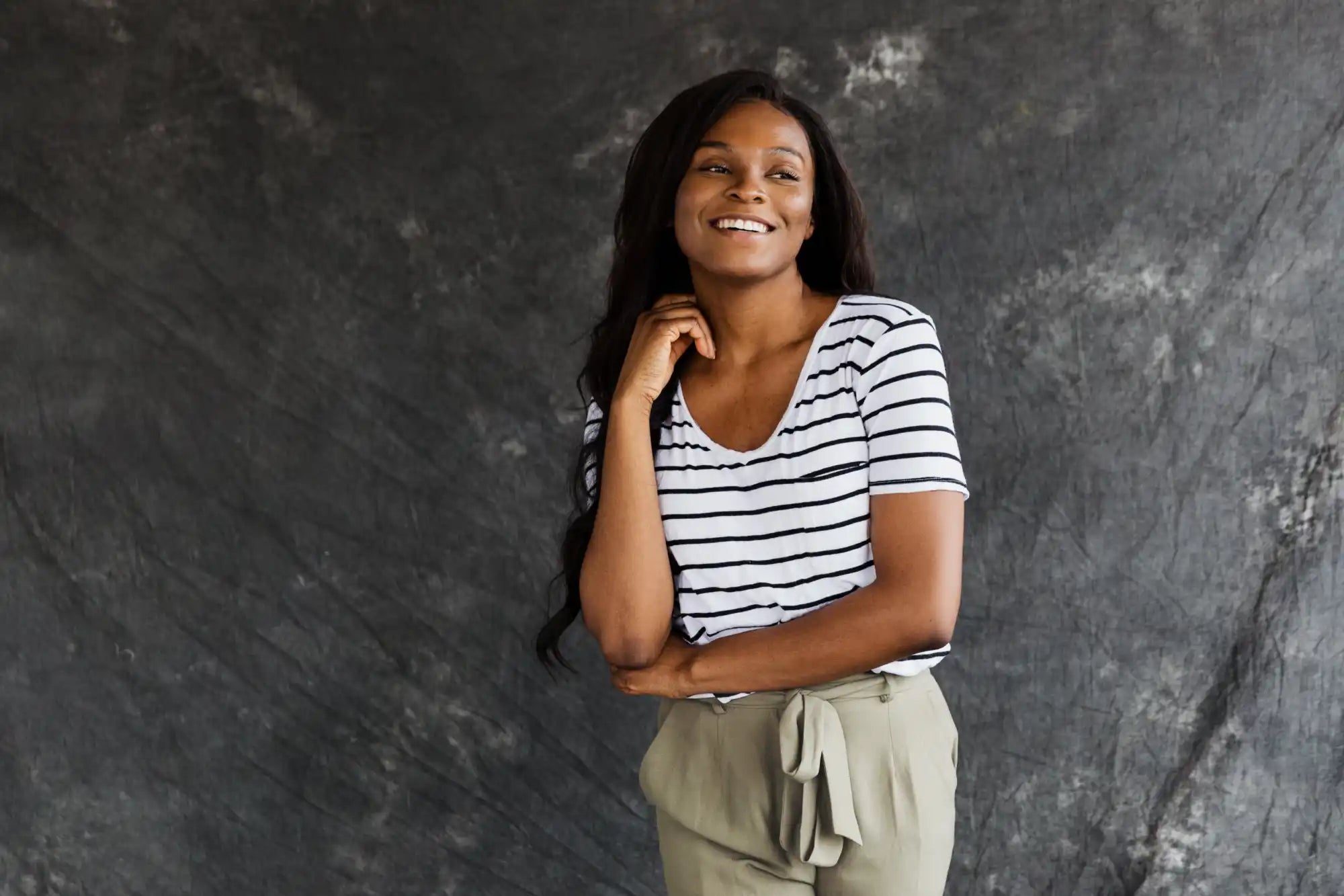 A person wearing a black and white striped t-shirt and khaki pants stands with a warm smile.