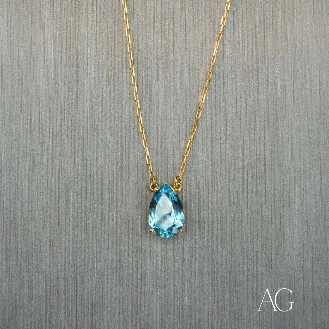 Gold necklace featuring a teardrop-shaped blue topaz pendant and 18 carat gold chain