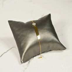 Solid gold kids ID bracelet with evil eye motif on a silver pillow display